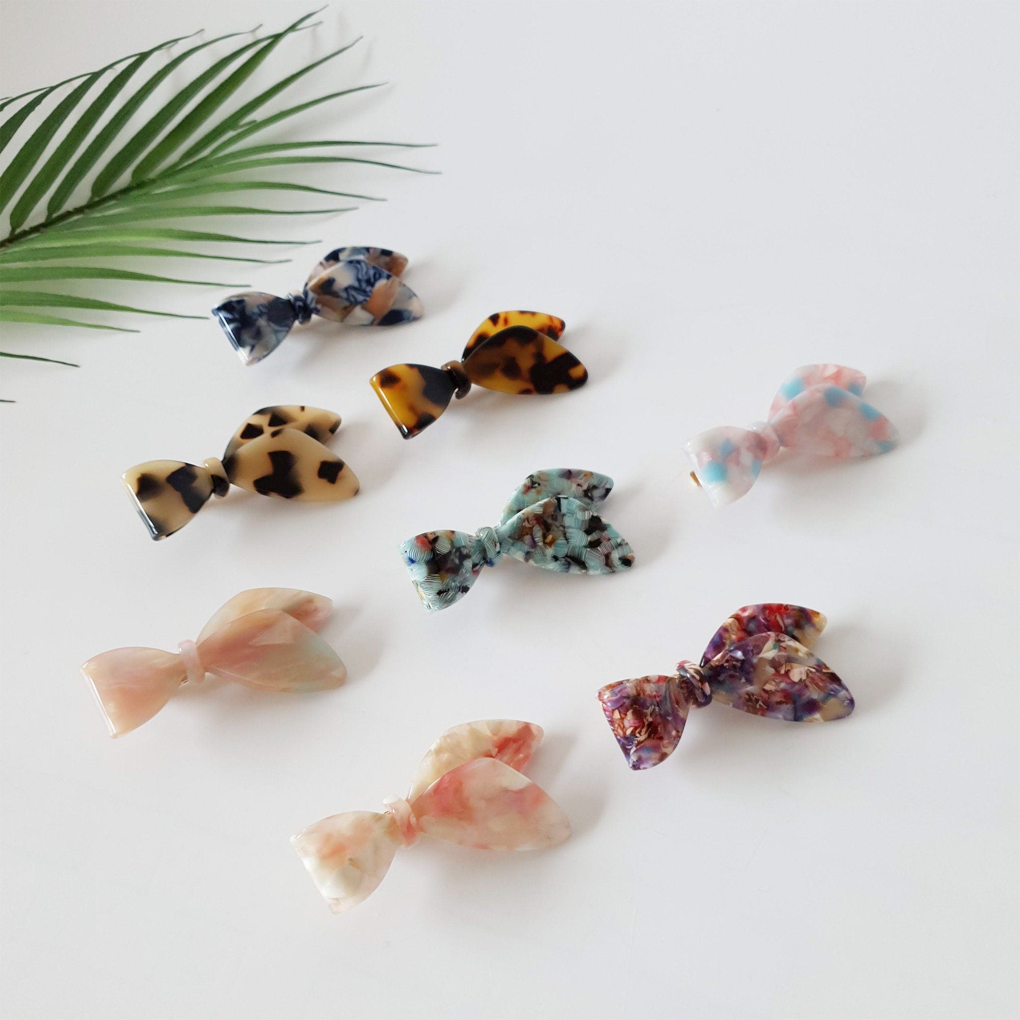 Cellulose acetate hair clip shaped like a tied scarf ribbon. Tortoise shell and marble pattern beak clip for side bangs or decorative accents.