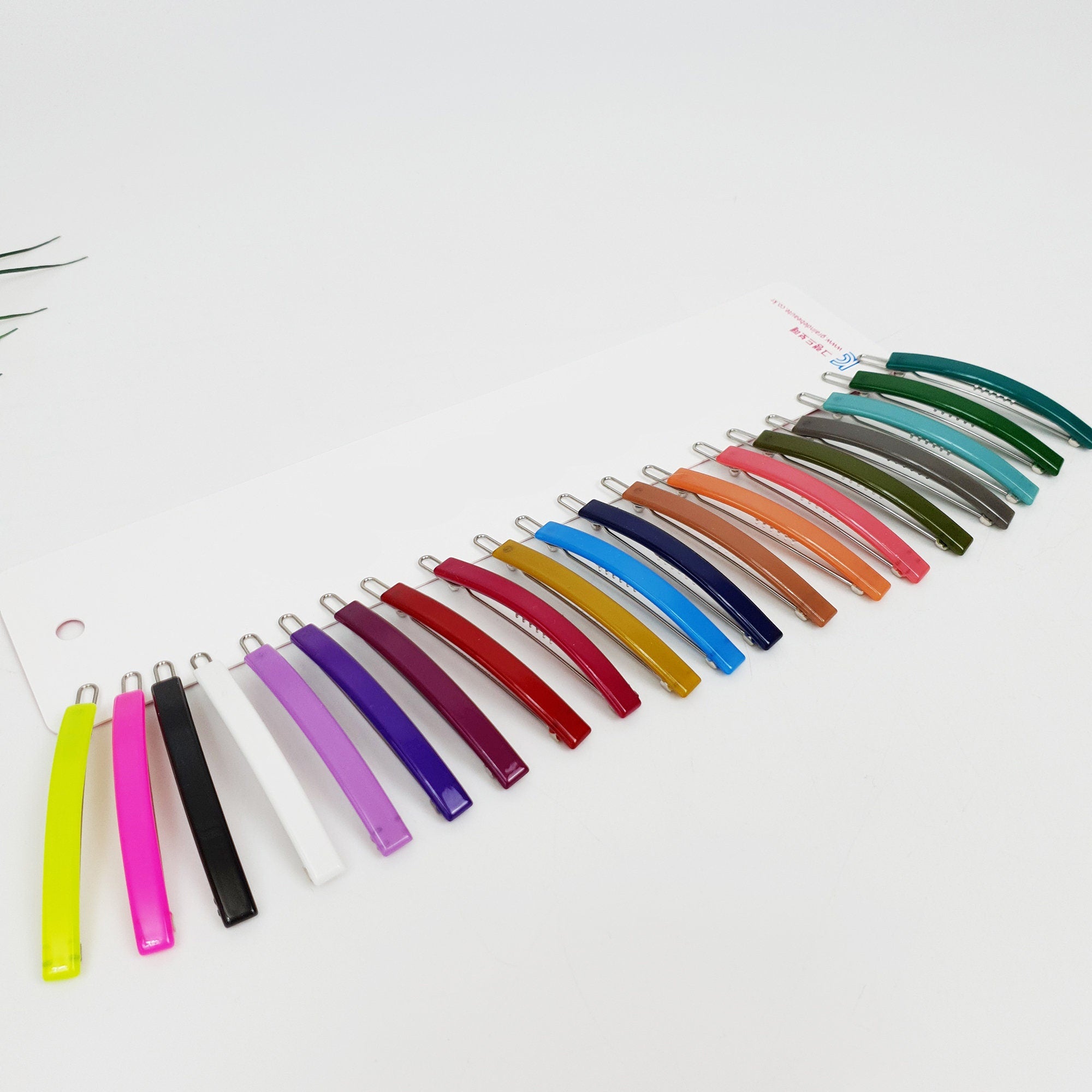 Slim rectangular cellulose acetate hair slide in vivid red. Minimalist straight bobby pin for side bangs, glossy hair accessory for thin hair. A set of twenty hair clips in various colors including green, blue, red, purple, pink, yellow, orange, brown, and white. The clips are arranged in a row on a white surface.