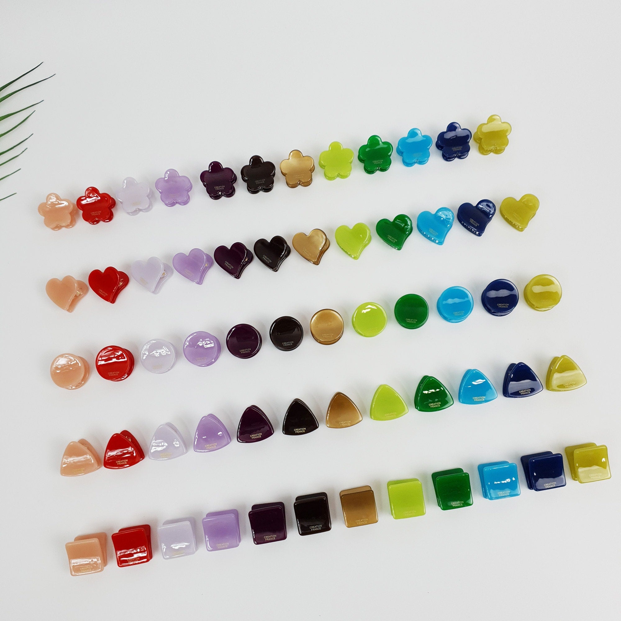 Tiny flower shaped cellulose acetate hair claw in vivid red. Mini geometric hair clip set (heart, circle, triangle, square) for styling bangs, Y2K colorful accessory. A collection of colorful plastic hair clips in various shapes, including flowers, hearts, circles, and triangles. The clips are arranged in rows on a white surface.