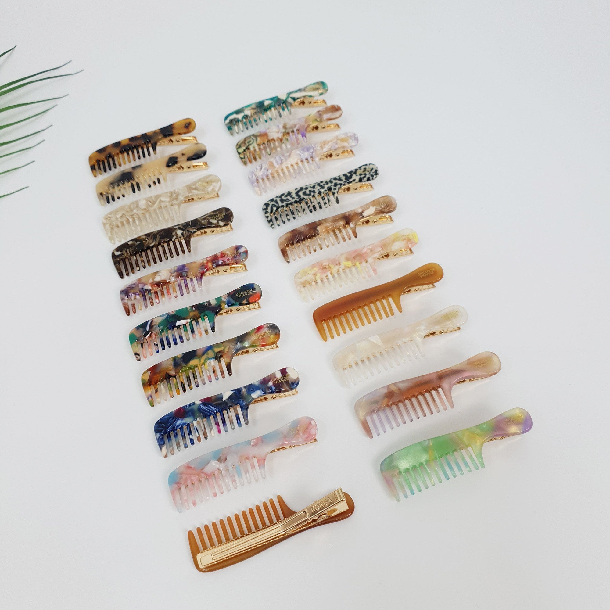 Cellulose acetate comb shaped hair clip in tortoise shell. Small side barrette for bangs and decorative styling. Cute Korean hair accessories gift. A collection of 17 colorful hair combs with gold clips. The combs are made of translucent plastic with different patterns and colors, including brown, white, black, green, blue, and pink. The combs are arranged in a row on a white surface.