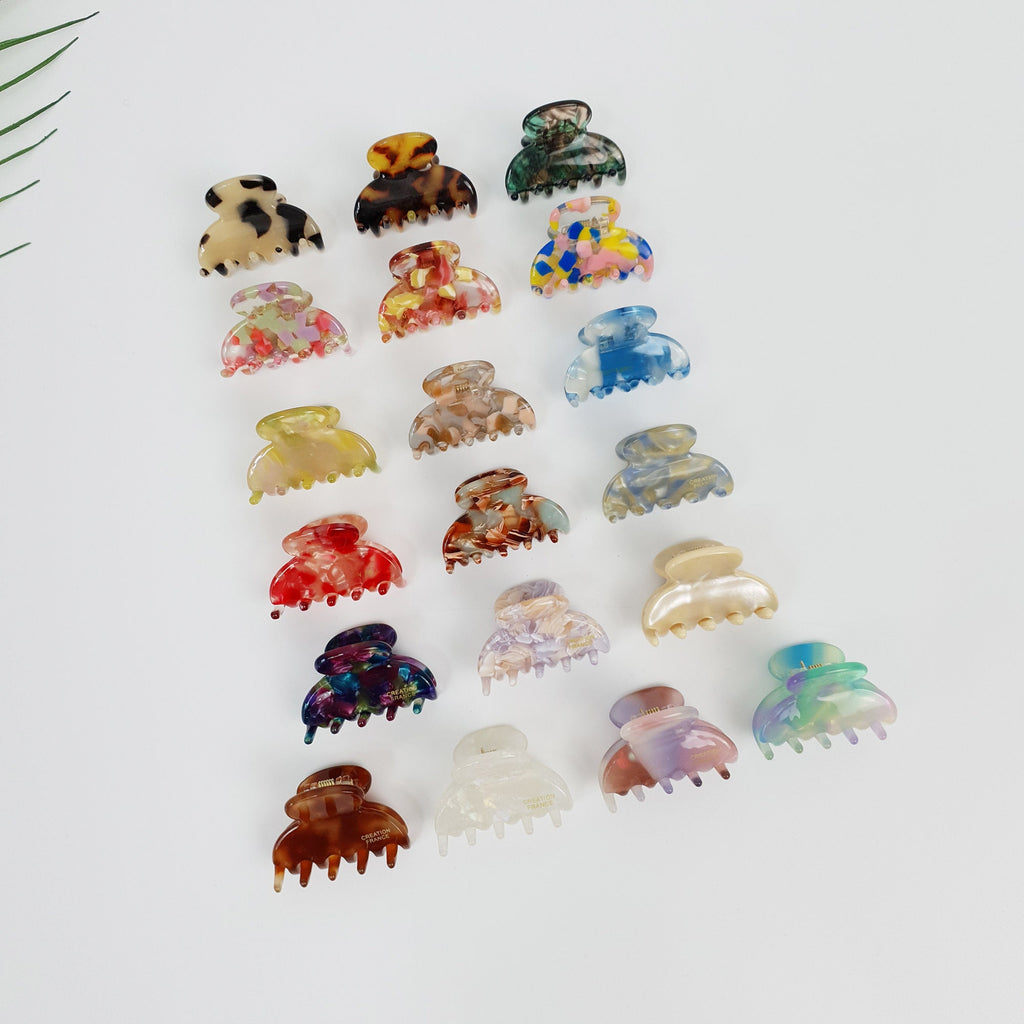 Cellulose acetate half moon mini hair claw clips in tortoise shell and marble patterns. Tiny semi-circle jaw clamps for toddler girls and women's side bangs. Cute small hair accessory. A collection of 18 colorful hair clips with various patterns and designs. The clips are made of plastic and have a claw-like shape. The colors include brown, black, white, blue, red, green, yellow, and pink.