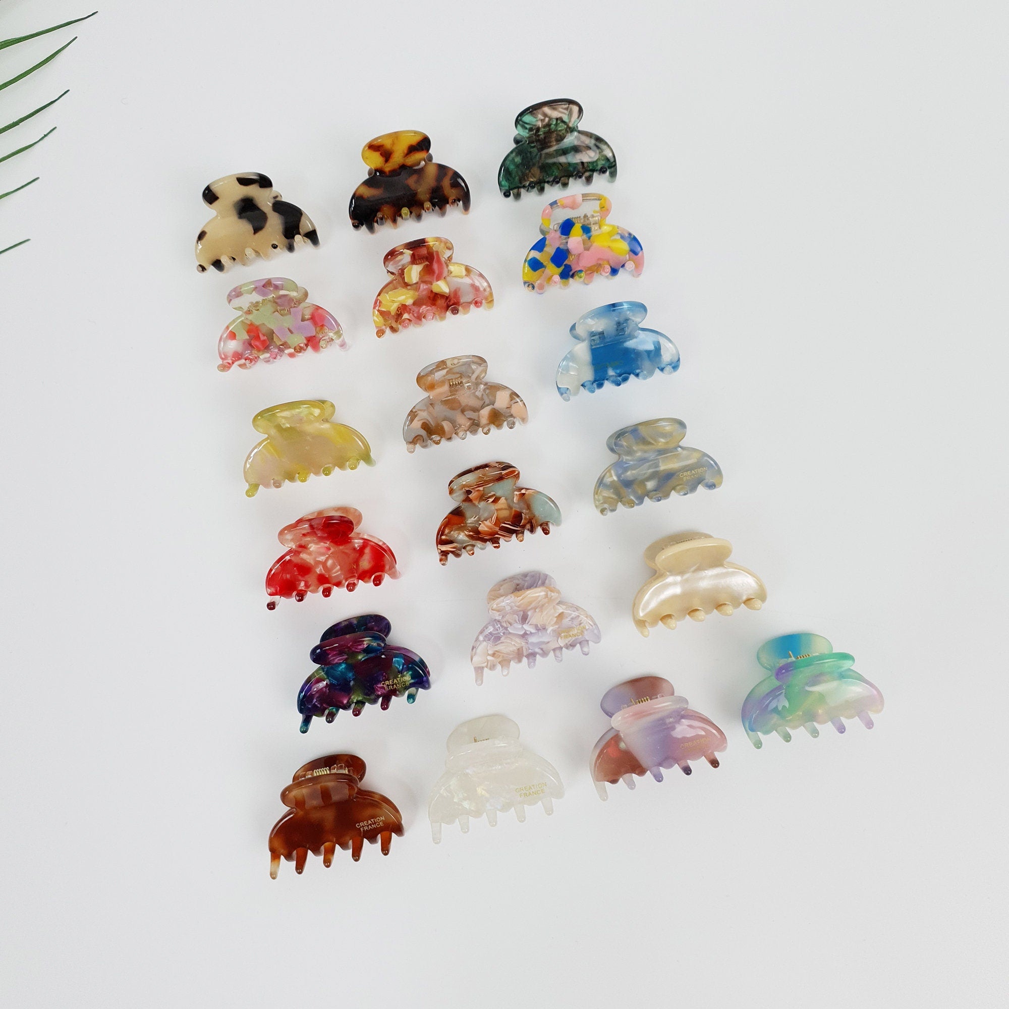 Cellulose acetate half moon mini hair claw clips in tortoise shell and marble patterns. Tiny semi-circle jaw clamps for toddler girls and women's side bangs. Cute small hair accessory. A collection of 18 colorful hair clips with various patterns and designs. The clips are made of plastic and have a claw-like shape. The colors include brown, black, white, blue, red, green, yellow, and pink.