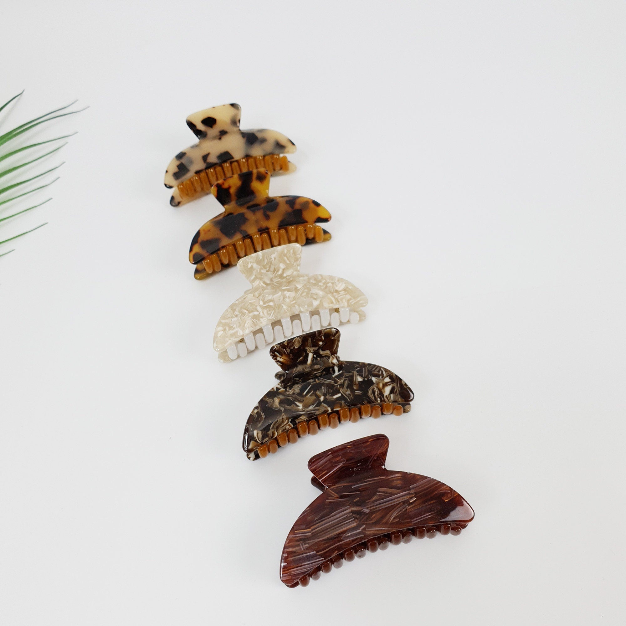 Cellulose acetate tortoise shell hair claw in semicircle shape. Double tooth clamp for thick hair and half-up styles. Marble leopard print hair accessories gift for her. Four different hair clips in various patterns. The clips are made of brown, black, and white plastic. The clips are arranged vertically in a row, with the brown clip at the top and the white clip at the bottom.