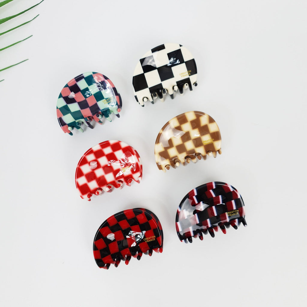 Cellulose acetate small hair claw clip featuring a retro checkerboard pattern. Semi-circular pebble shaped mini jaw clip in black and white check for half up hairstyles.