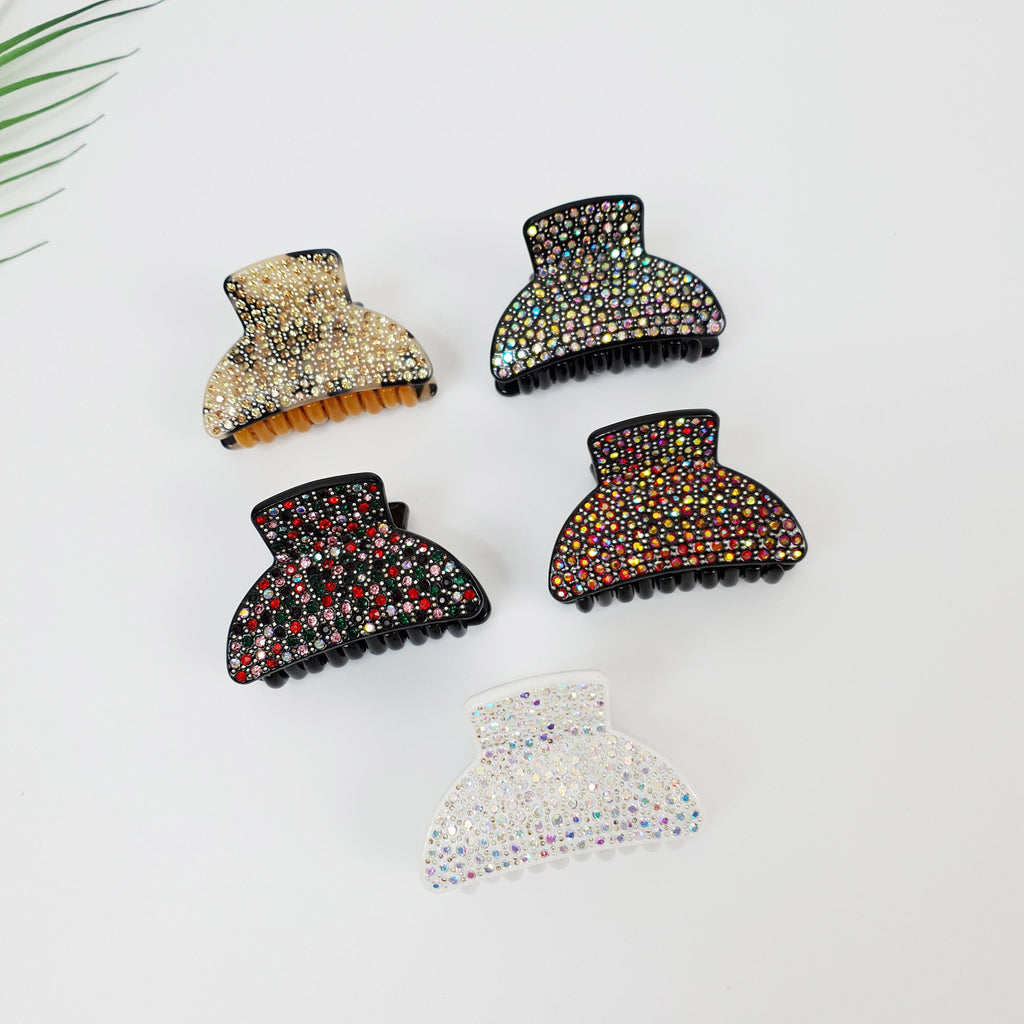 Small rhinestone hair claw clip in acetate material with sparkling crystal details. Half moon jaw clip with double teeth grip for thick or thin hair styling. Four black hair clips with different colored rhinestones. The clips are in the shape of a half circle and have a row of teeth on the bottom. The rhinestones are in a variety of colors, including gold, red, green, and white.