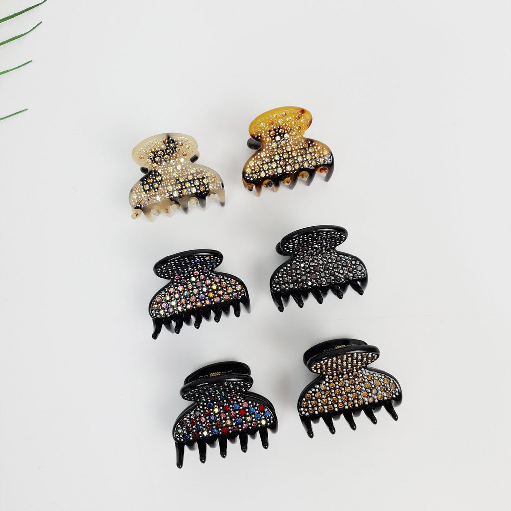 Cellulose acetate mini hair claw clip half moon shape with crystal rhinestones for women side bangs and wedding guest style. Five hair clips with rhinestones. Two clips are brown with gold rhinestones, two clips are black with multi-colored rhinestones, and one clip is black with blue and red rhinestones.