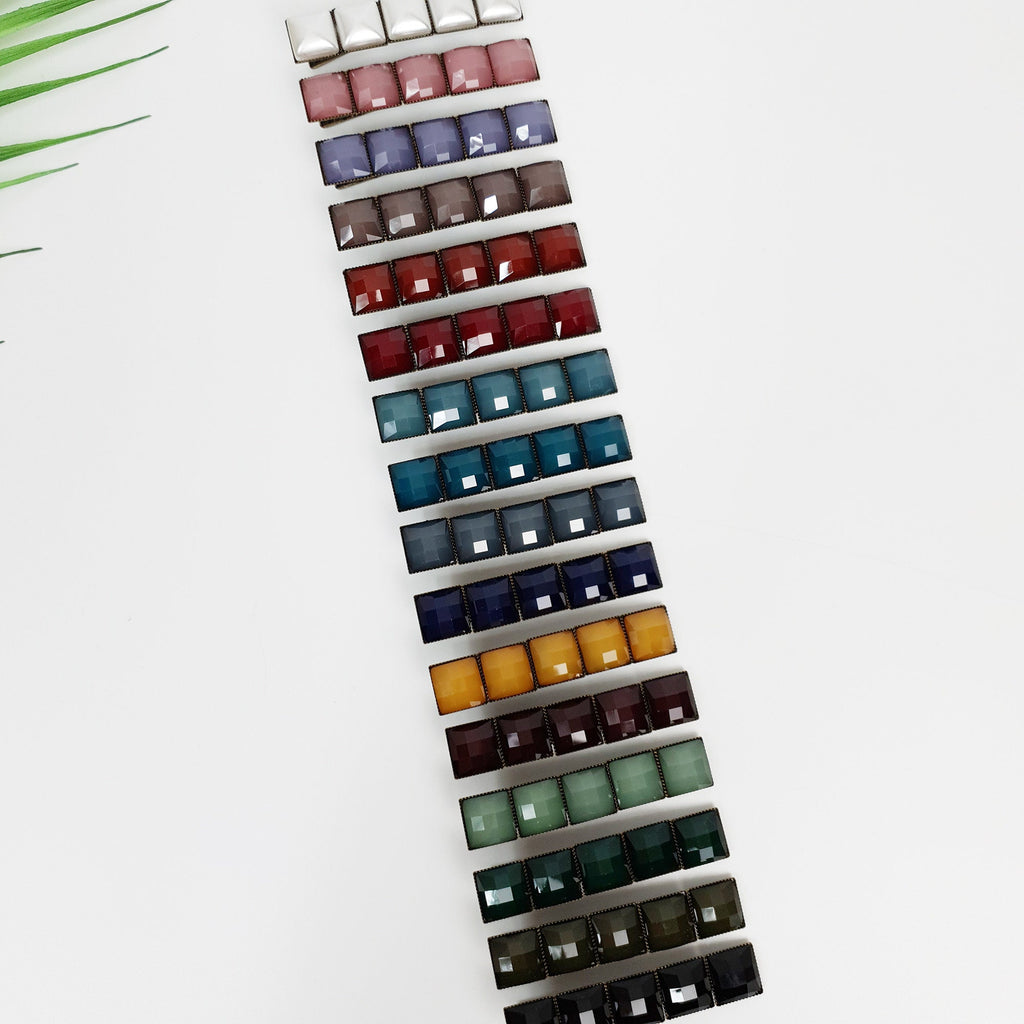 Vintage style square tile hair clip with antique brass finish. 2.4 inch mosaic alligator clip for side bangs and retro hairstyles. A set of 16 hair clips with square-shaped gems in various colors, including white, gray, brown, red, blue, green, and yellow. The clips are arranged vertically in a row, with the white gem at the top and the yellow gem at the bottom.