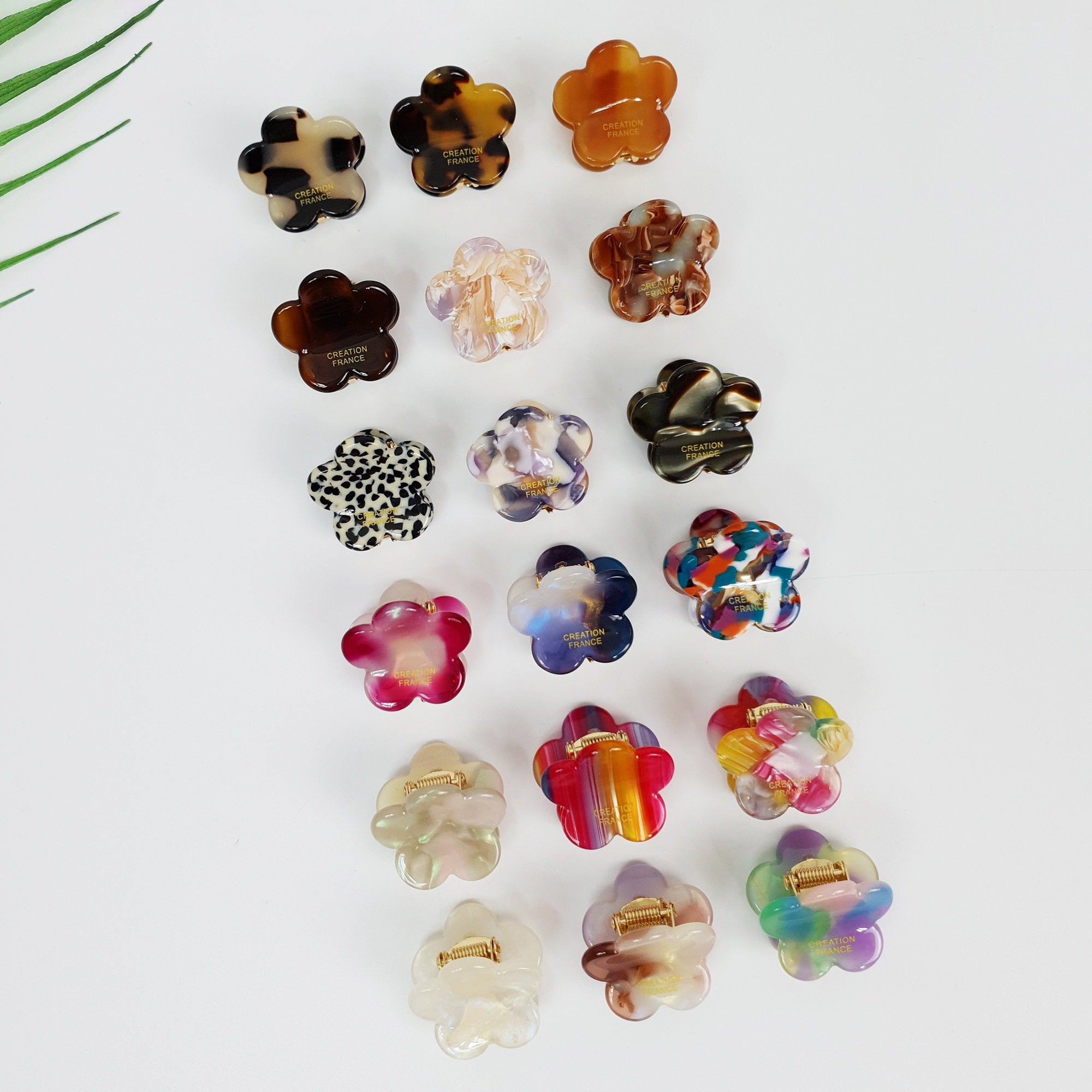 Miniature cellulose acetate hair claw in tortoise and pastel colors, 2.5cm daisy flower shape for styling bangs, non-slip tiny jaw clip for side hair. A collection of 15 colorful flower-shaped hair clips. The clips are made of plastic and have a variety of patterns, including leopard print, stripes, and swirls. The clips are all in different colors, including pink, purple, blue, green, orange, and brown. The clips have the words 'CREATION FRANCE' printed on them.