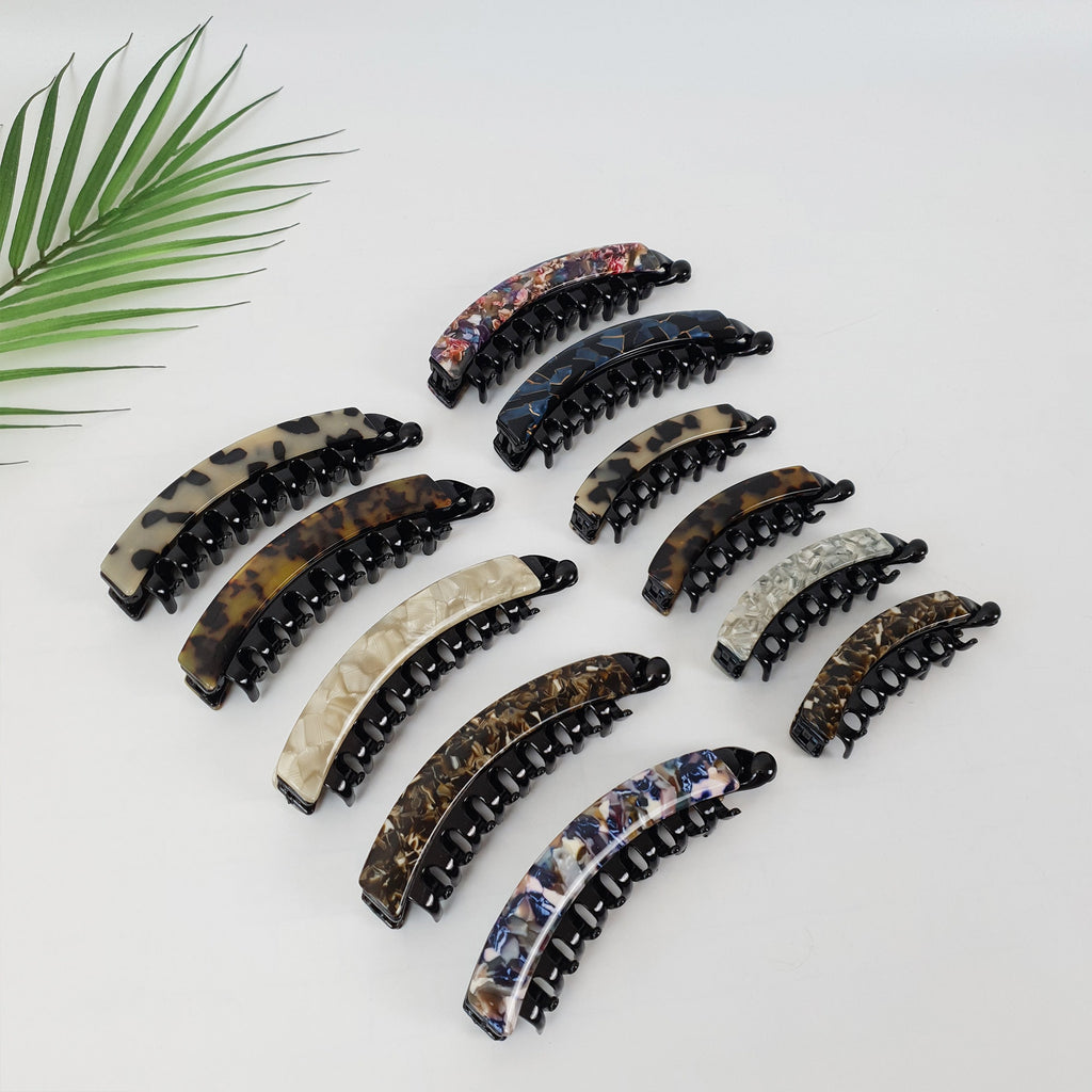 Cellulose acetate banana hair clip in tortoise and checkered patterns, interlocking clincher comb for ponytails, durable styling tool for thick or fine hair. A collection of ten black and brown patterned hair clips. The clips are all in the shape of a half-circle and have a row of teeth on the inside to hold hair in place.