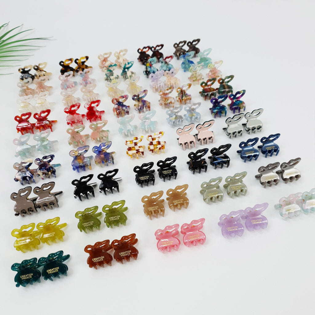 Set of 2 miniature cellulose acetate butterfly hair clips, 2cm tiny jaw claws in tortoise shell and pastel colors, cute non-slip bangs holder for girls and women. A collection of colorful plastic hair clips shaped like bunnies. The clips have a variety of patterns and colors, including pink, blue, green, brown, and black. The clips have the words 'Creation France' printed on them.