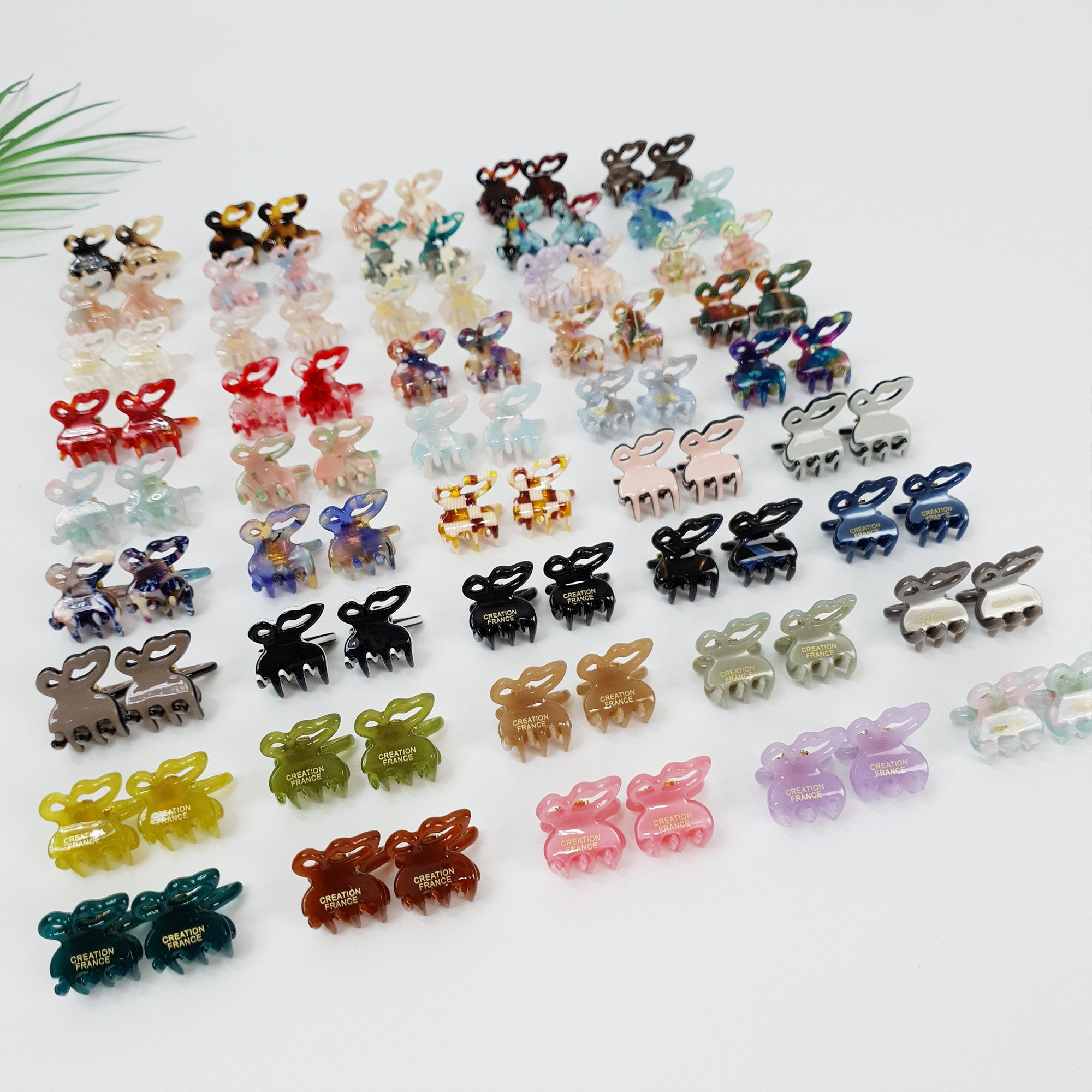 Set of 2 miniature cellulose acetate butterfly hair clips, 2cm tiny jaw claws in tortoise shell and pastel colors, cute non-slip bangs holder for girls and women. A collection of colorful plastic hair clips shaped like bunnies. The clips have a variety of patterns and colors, including pink, blue, green, brown, and black. The clips have the words 'Creation France' printed on them.