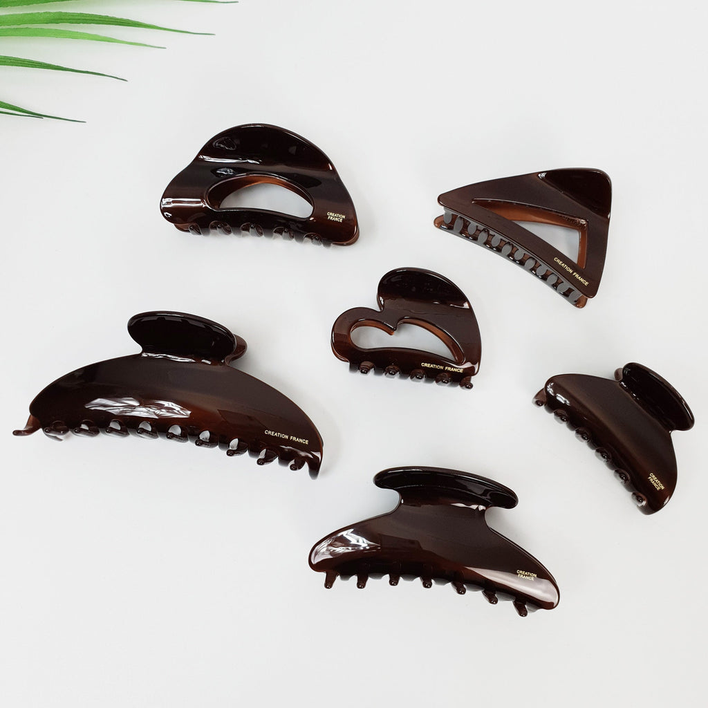 Chic brown cellulose acetate hair claw clips in geometric shapes including heart triangle and half moon, minimalist hair accessories for women. Six brown plastic hair clips with a gold inscription that reads 'CREATION FRANCE'. The hair clips are in various shapes, including a heart, a triangle, and a rounded rectangle.