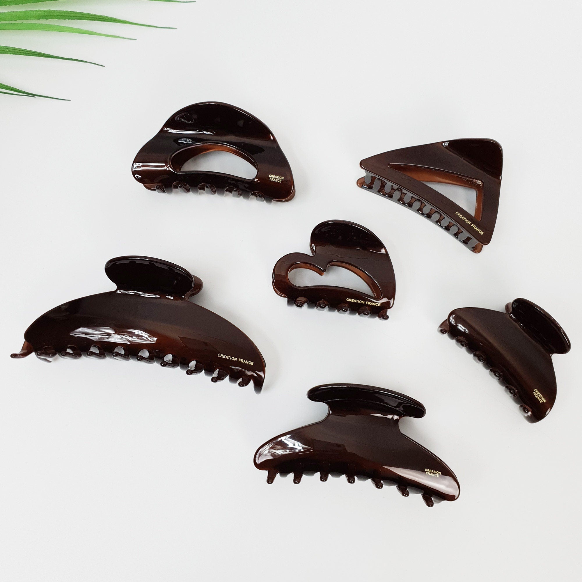 Chic brown cellulose acetate hair claw clips in geometric shapes including heart triangle and half moon, minimalist hair accessories for women. Six brown plastic hair clips with a gold inscription that reads 'CREATION FRANCE'. The hair clips are in various shapes, including a heart, a triangle, and a rounded rectangle.
