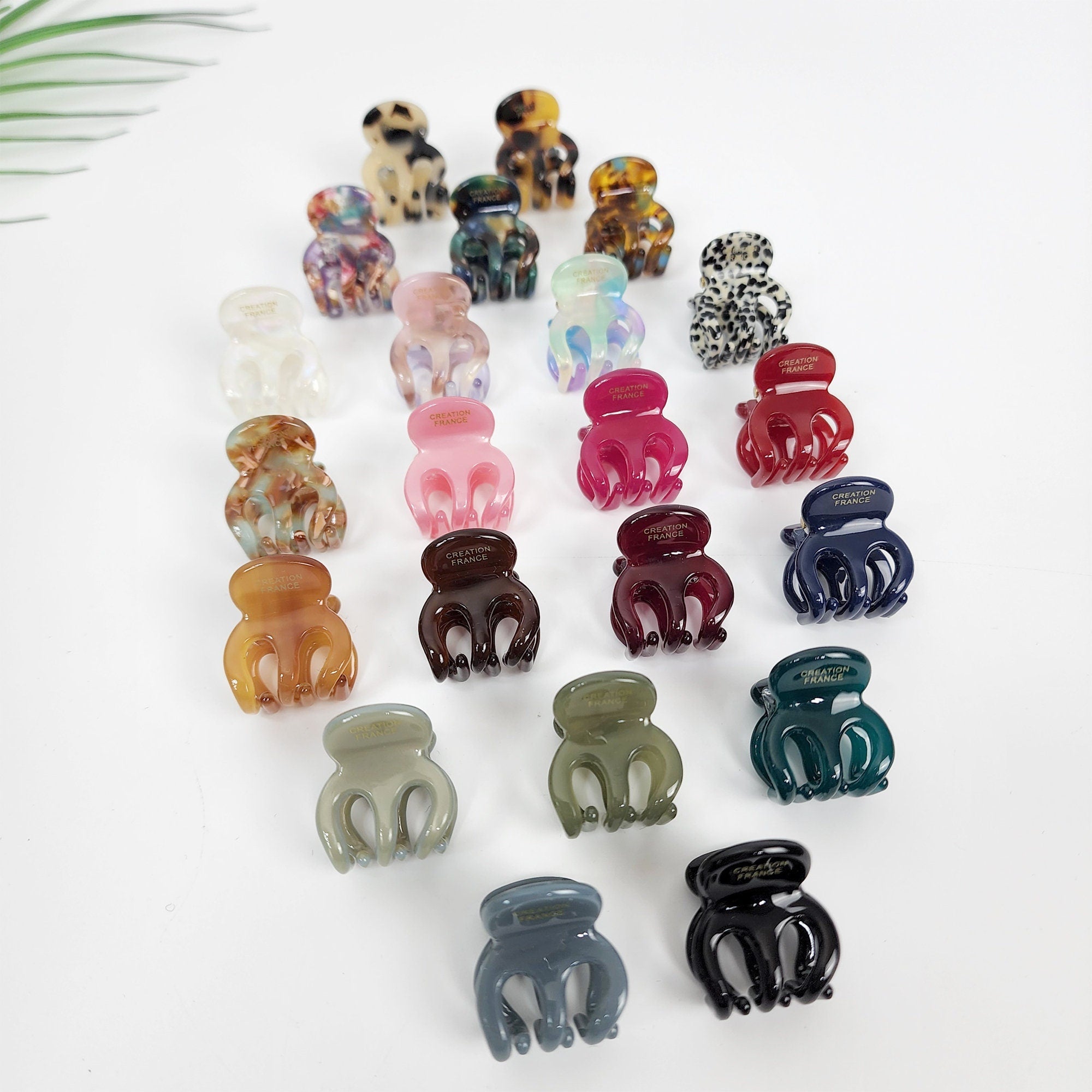 Tiny cellulose acetate jaw clips in tortoise shell and pastel solids, 0.8 inch rectangular block shape for styling bangs or fine hair. A collection of twenty-two assorted plastic hair clips in various colors and patterns. The clips are all in the shape of a claw with three prongs. The clips have the words 'Creation France' printed on them.
