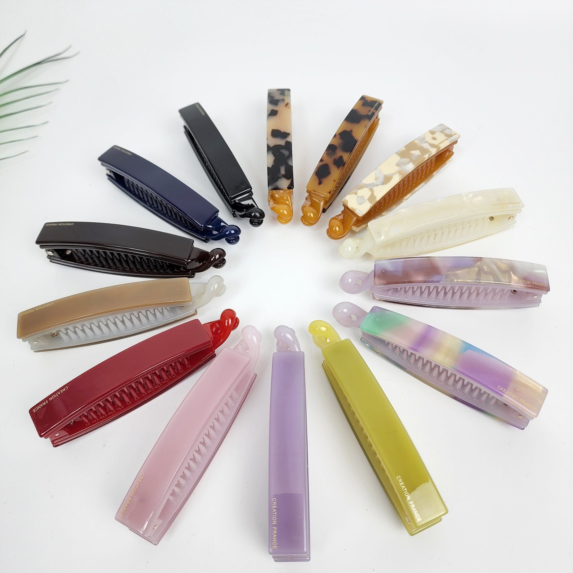 Leopard long square banana claw clip in tortoise shell and solid colors. 3.9 inch medium hair comb barrette for women's ponytail styling. Simple Korean hair accessory. Assortment of hair clips in various colors and patterns, including tortoise shell, brown, black, white, red, pink, purple, and green. Some clips have the words 'Creation Paris' printed on them.