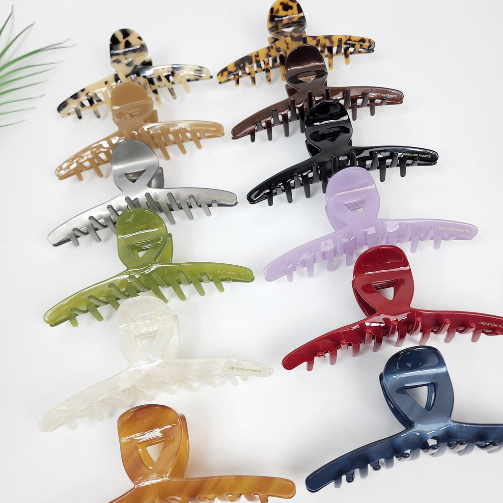 Large cellulose acetate hair claw clip for thick hair. Tortoise shell and solid color french twist jaw clamp. 5.2 inch jumbo accessory for elegant updos and buns.  A collection of ten assorted plastic hair claw clips. The clips are in various colors including brown, black, silver, green, white, purple, and blue. The clips have a unique design with a curved shape and multiple teeth.