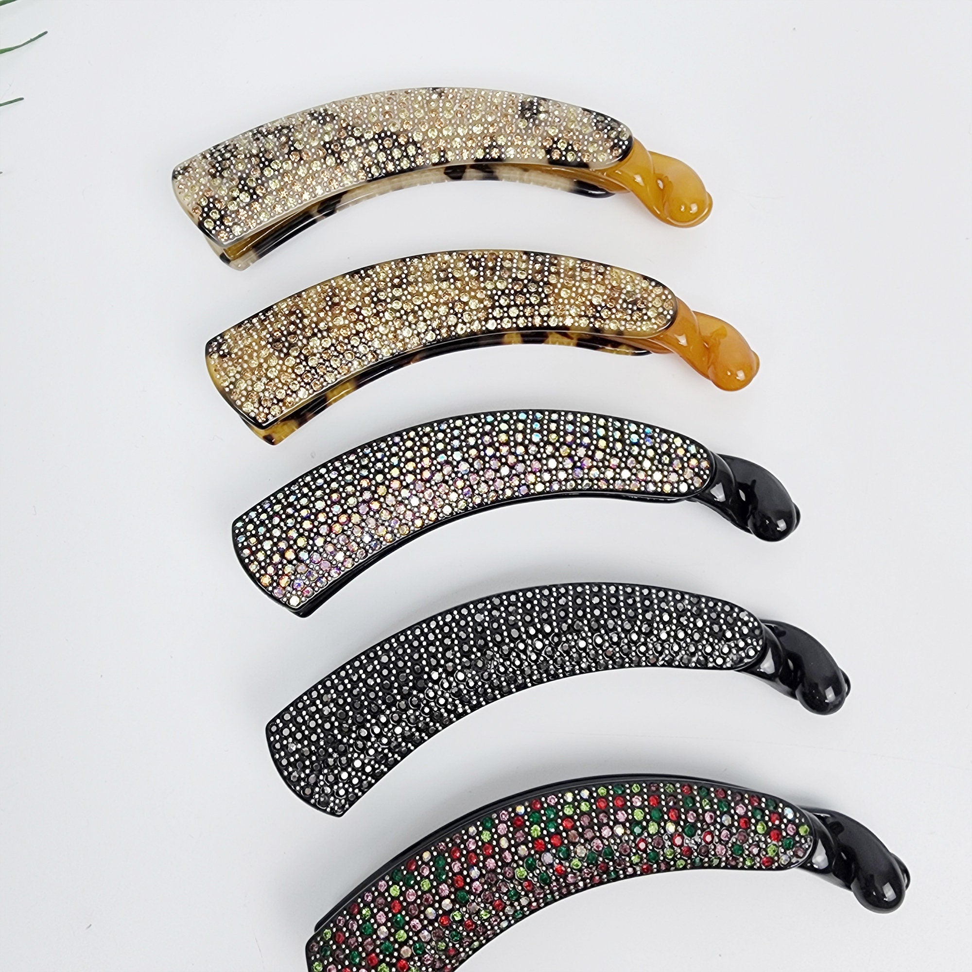 Cellulose acetate banana clip with rhinestones. Large 4.9 inch sparkly hair comb for secure ponytails and updos.  Four decorative hair clips with rhinestones. The clips are curved and have a shiny finish. The clips are in different colors, including black, brown, and clear.