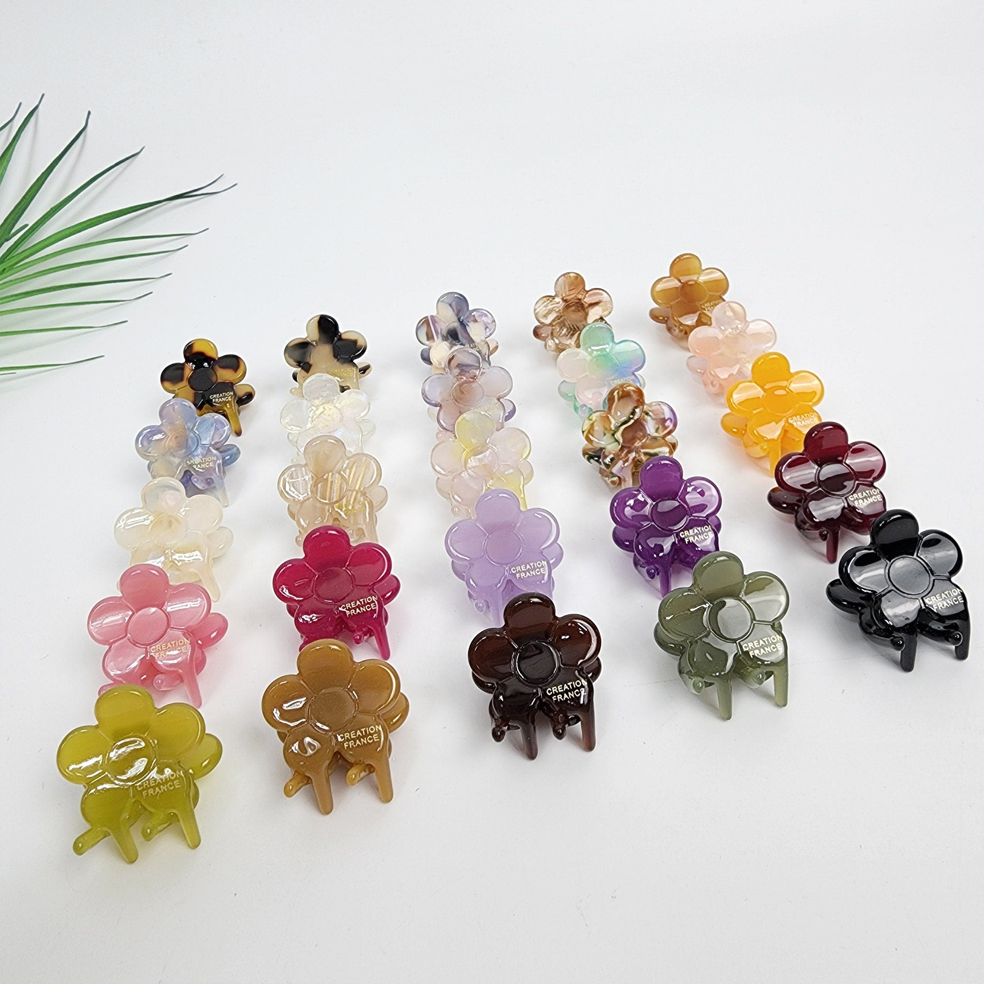 Small acetate flower hair claws in tortoise shell and pastel colors 5 petal floral mini clip for bangs styling. Assortment of colorful flower-shaped hair clips with the words 'Creation France' printed on the bottom of each clip.