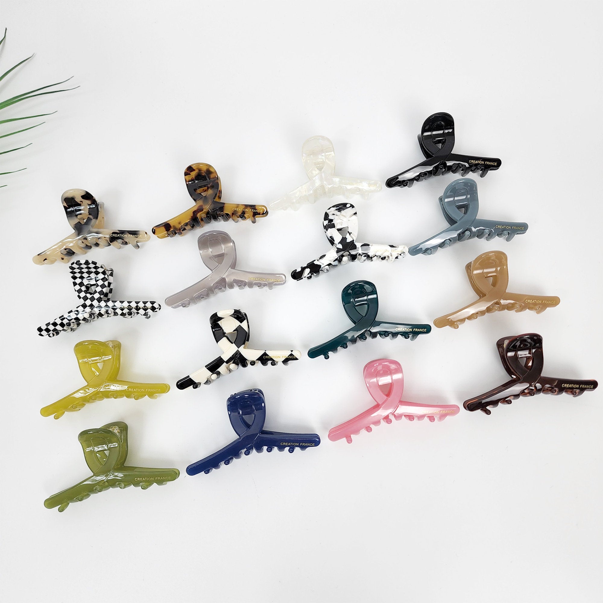 Twisted cellulose acetate hair claw clip in tortoise shell and checkerboard patterns. 2.8 inch small jaw clamp for half-up hairstyles. A collection of 15 plastic hair clips in various colors including black, white, brown, green, blue, and pink. The clips are all the same shape and have a checkered pattern. The clips are arranged in a semi-circle on a white background.