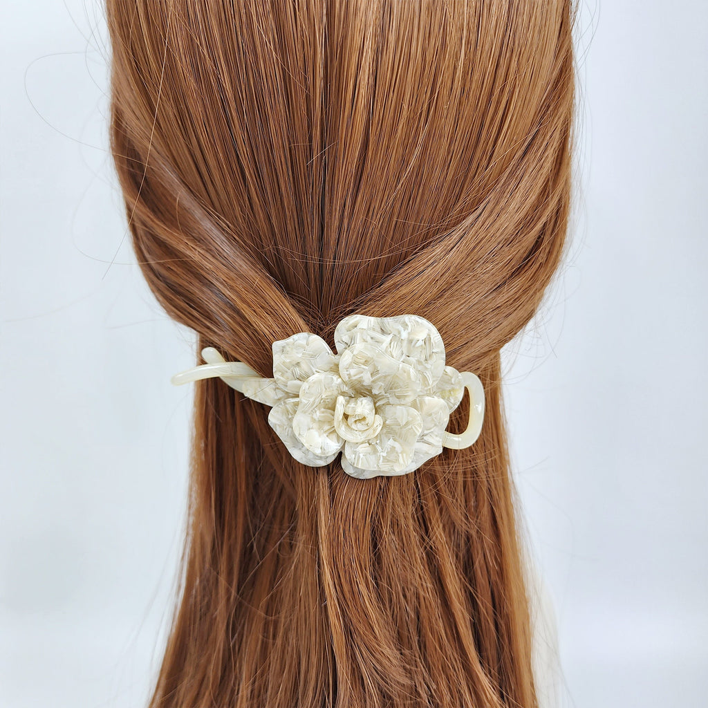 Cellulose acetate flower banana clip in tortoise shell and marble patterns for elegant ponytail styling. A white flower hair clip with a pearl-like finish. The clip is made of plastic and has a simple design. The clip is worn in a woman's brown hair.