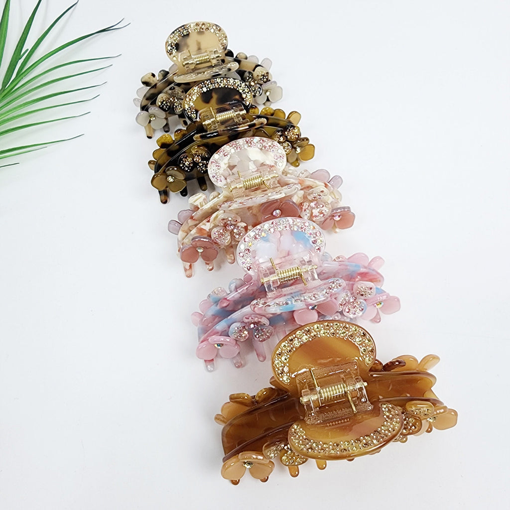 Cellulose acetate hair claw clip with rhinestone flower details and tortoise shell pattern for thick hair styling Six hair claw clips in various colors and patterns. The clips are made of plastic and have a shiny finish. The clips are decorated with rhinestones and small flowers. The clips are arranged vertically, with the largest clip at the top and the smallest clip at the bottom.
