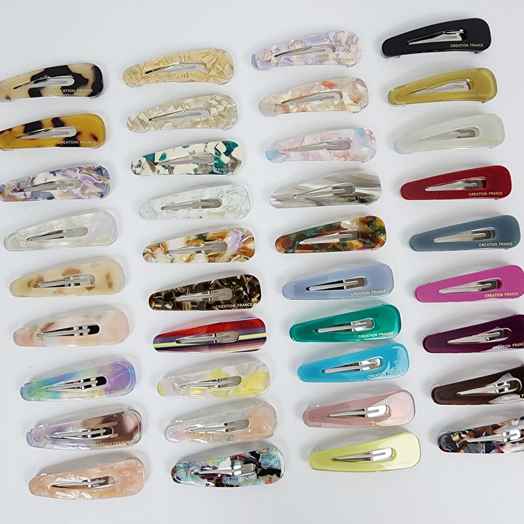 Cellulose acetate triangle hair slides in minimalist tortoise and marble patterns for women, featuring a sturdy snap mechanism for side bangs styling.