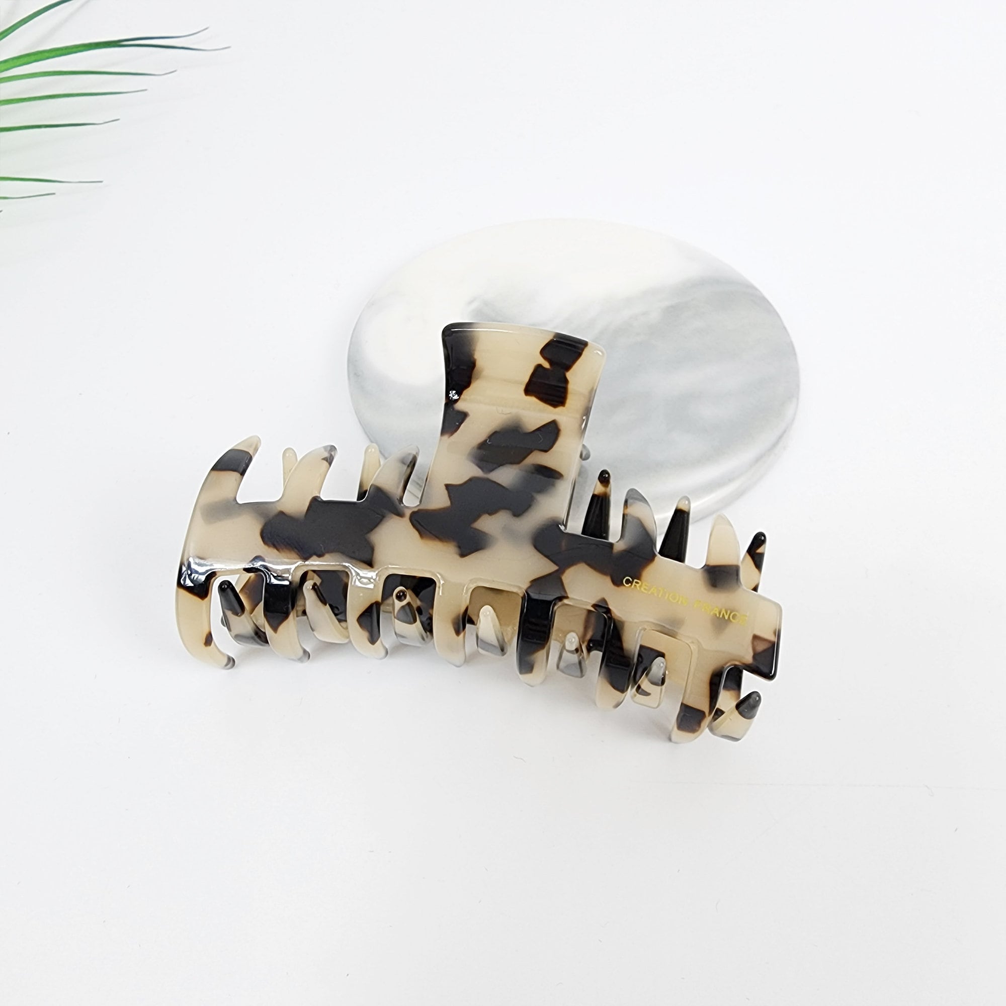 Tortoise shell acetate claw clip with spike teeth design, 3.5 inch medium hair jaw clip for french twist updo and half-up styling. A large, brown and white tortoise shell hair claw with a gold inscription that reads 'CREATIVE FRANCE'. The claw is designed with multiple teeth to hold hair securely.