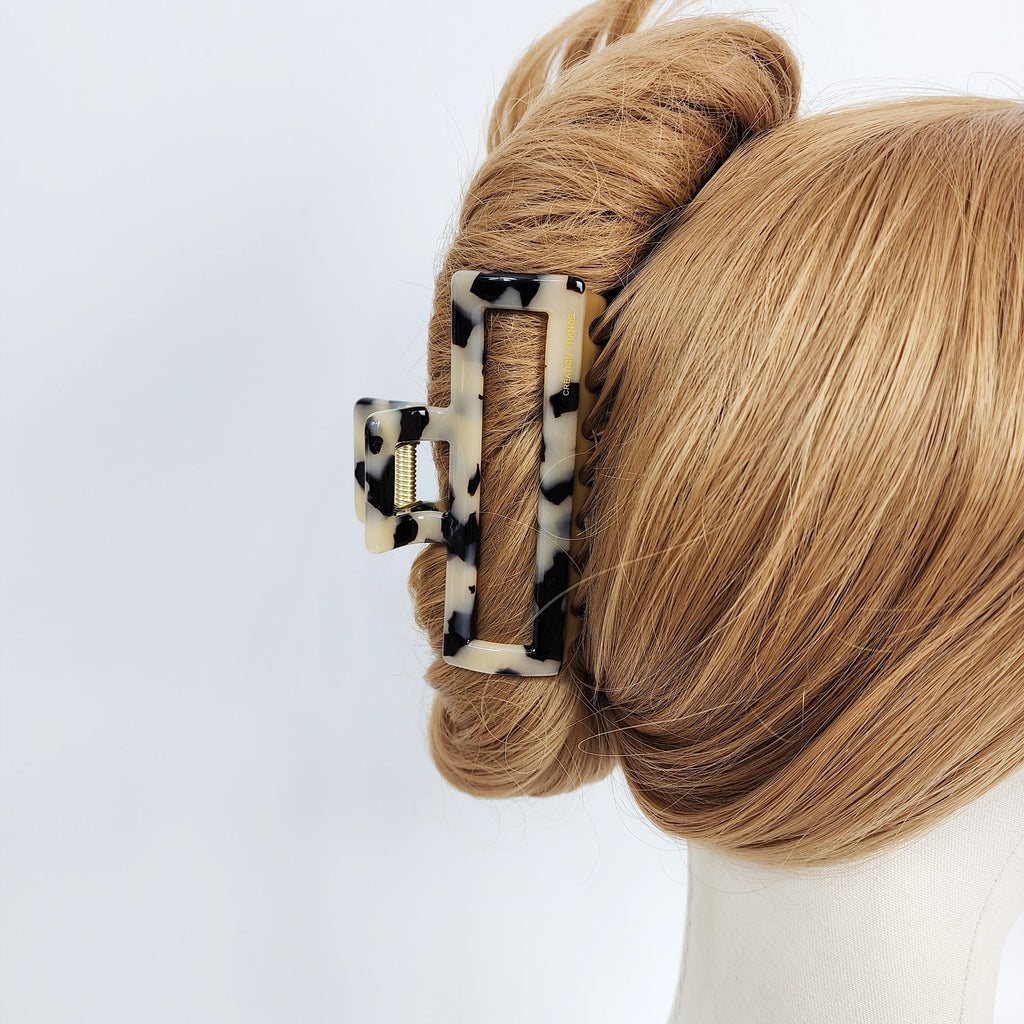 Cellulose acetate rectangular hair claw in tortoise shell and solid colors featuring a U-wire mechanism for thick hair styling and secure updos. A black and white patterned hair claw clip. The clip is made of plastic and has a rectangular shape. The clip is designed to hold hair in place.