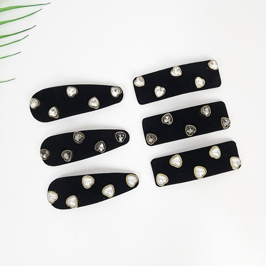 Black velvet snap hair clip with heart shaped pearls and rhinestone details for side bangs styling.  Five black velvet hair clips with gold trim and clear rhinestone hearts. The clips are arranged in two rows, with three clips in the top row and two clips in the bottom row.