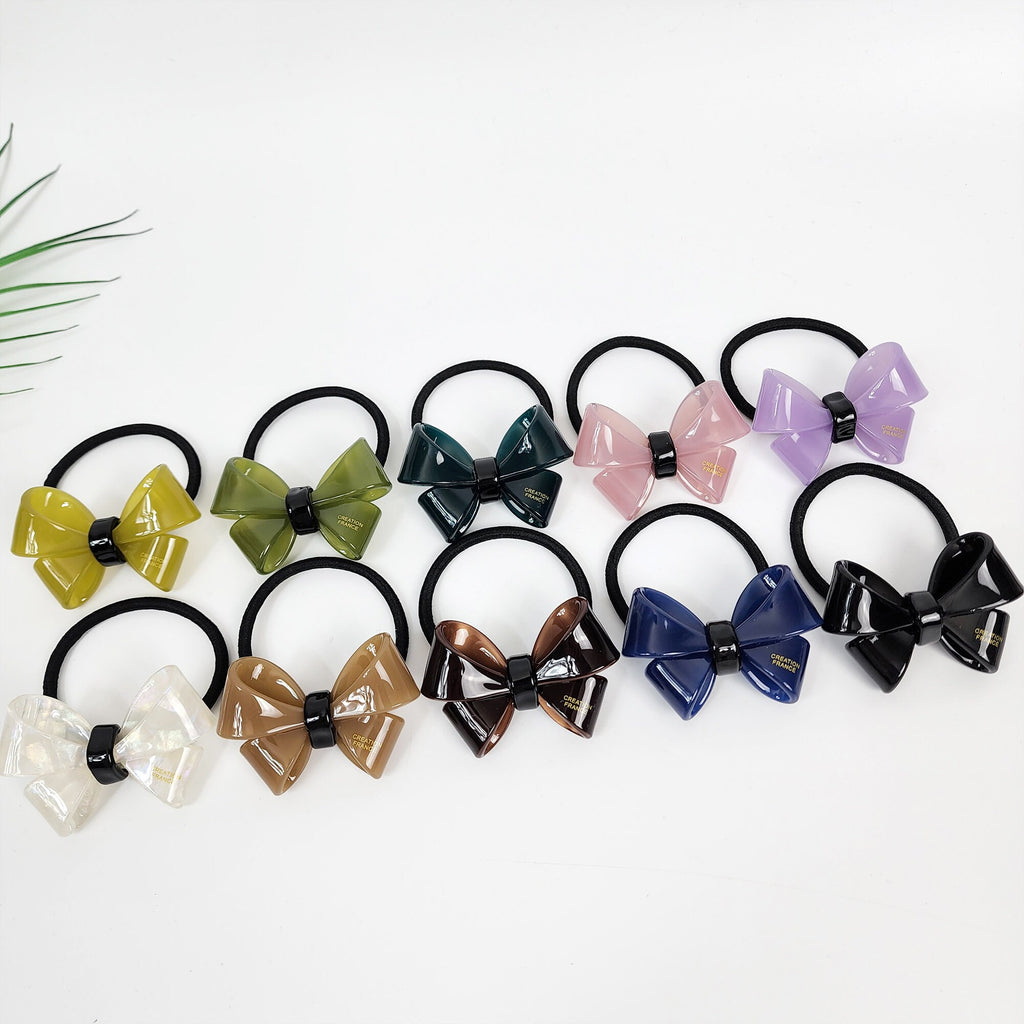 Large cellulose acetate butterfly ribbon hair tie. Glossy 3D bow ponytail holder in aurora and pure colors for women birthday gifts. Korean fashion accessory with thick elastic band. Ten assorted hair scrunchies with bows in various colors including green, brown, blue, pink, and white. The bows are made of a translucent material and have a black center.