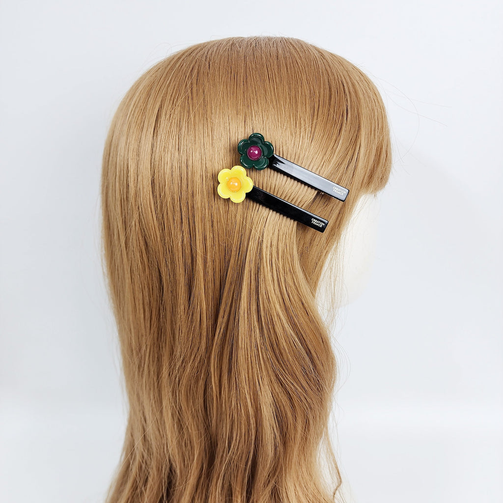 Cellulose acetate alligator clip with small daisy flower. 2.8 inch cute side hair pin for bangs. Minimalist glossy accessory available in pink and black. Two black hair clips with yellow and green flower accents. The flowers have a red center.