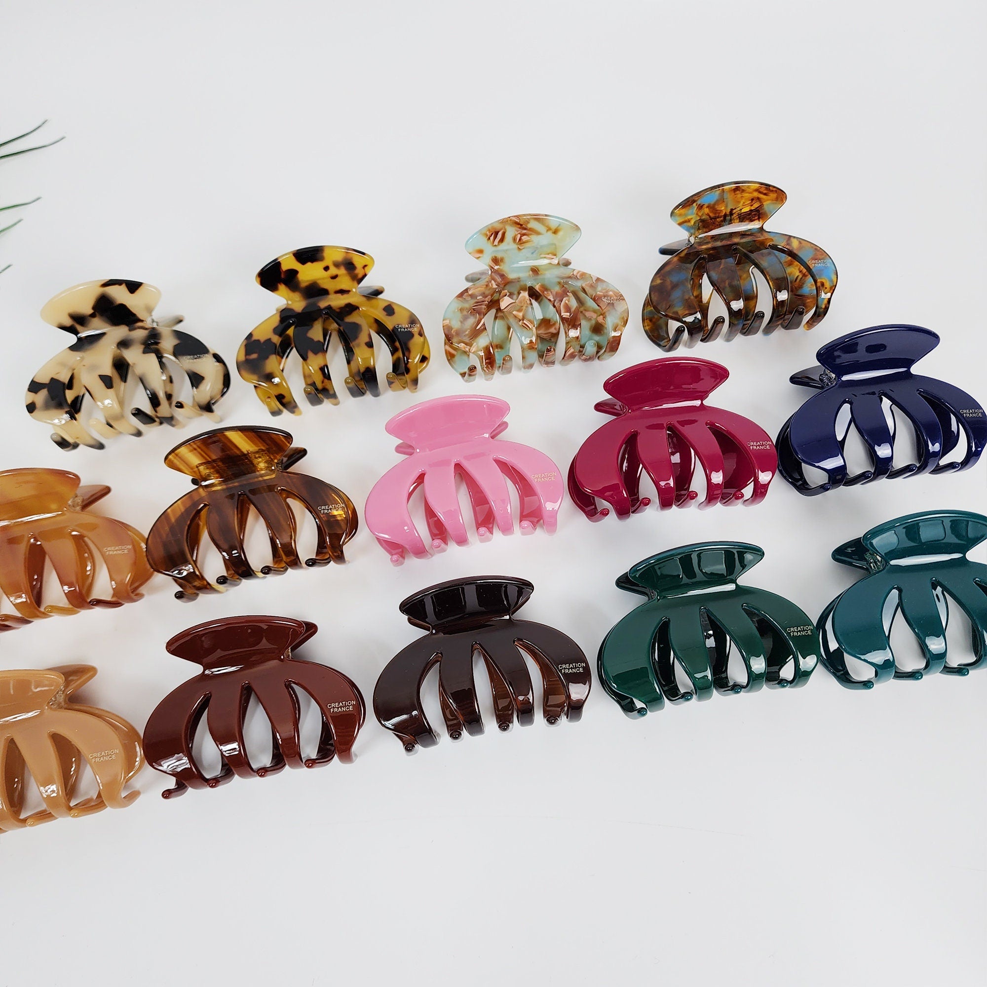 Small cellulose acetate hair claw clip in pumpkin shape and tortoise shell pattern. Cute 2.4 inch jaw clip for half updo styling. Assortment of hair clips in various colors and patterns, including brown tortoise shell, green, pink, and blue. The clips are all claw shaped and have a decorative design.