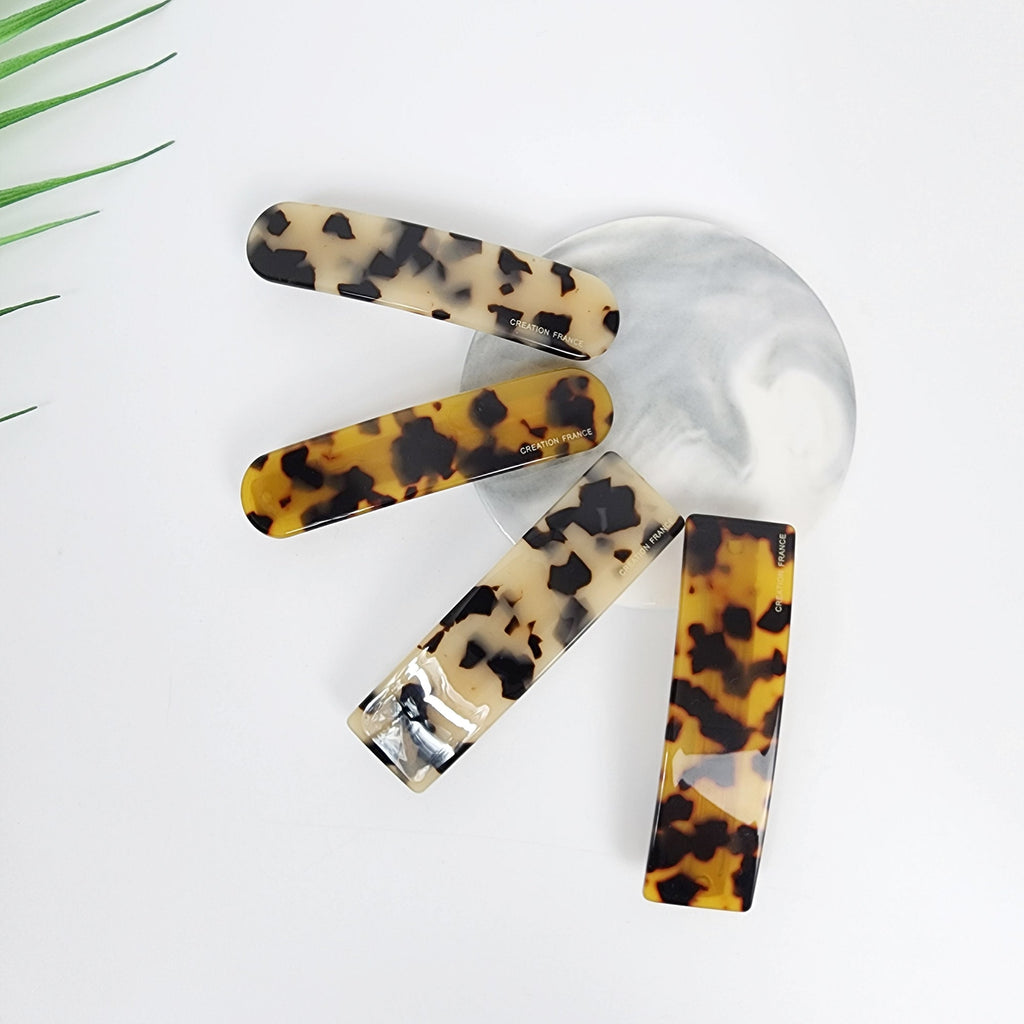 Cellulose acetate rectangular hair barrette in brown tortoise shell pattern. Minimalist 3.5 inch french style hair clip for women holding side hair or half up hairstyle. Four tortoiseshell hair clips with a rectangular shape. The clips are made of a brown and cream plastic material with a mottled pattern. The clips have the words 'CREATION FRANCE' printed on them.
