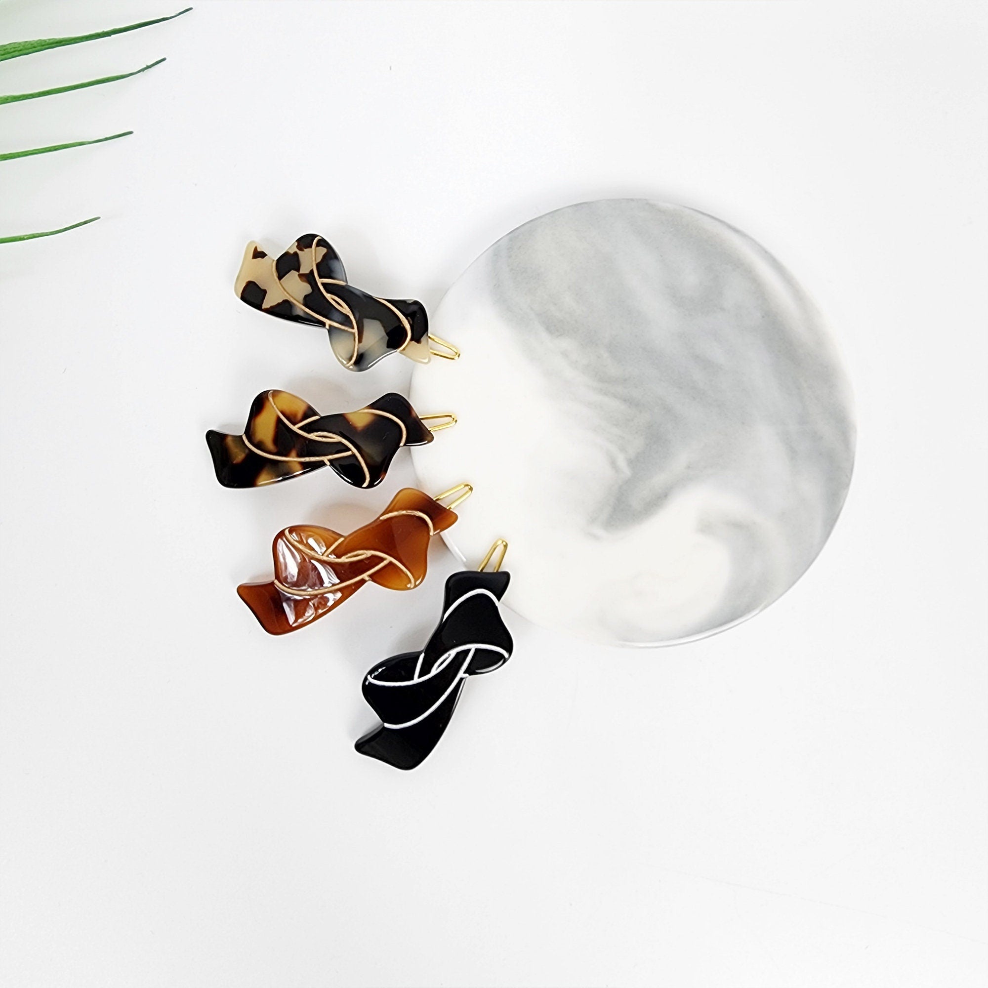 Acetate tortoise shell snap clip with gold wire. Small 1.8 inch ribbon hair pin for bangs. Minimalist Korean hair accessory. Four hair clips in the shape of a bow. The clips are made of brown, black, and tortoise shell plastic. The clips have a gold wire detail.