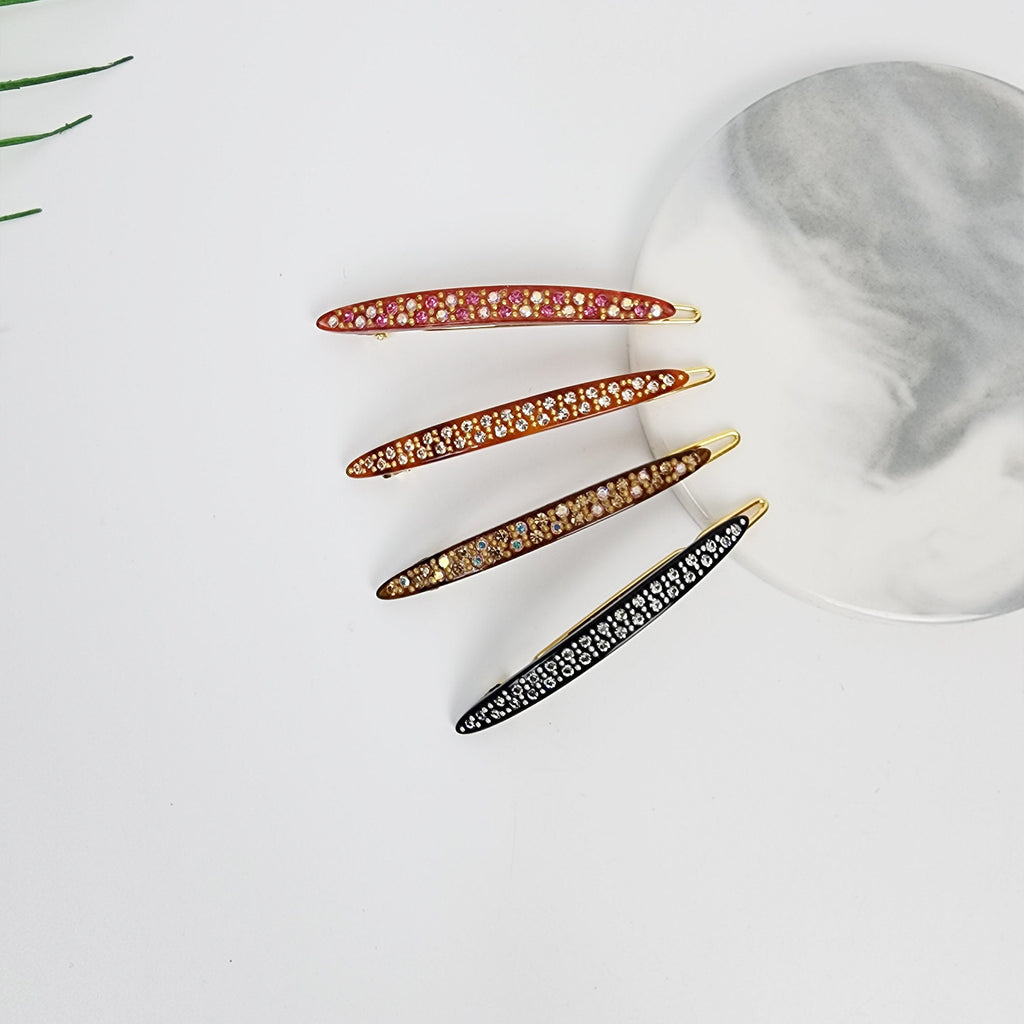 Cellulose Acetate Slim Snap Clip with Crystal Embellishments Long Oval Barrette for Bangs Tortoise Shell Pattern Korean Hair Accessory Four jeweled hair clips in varying colors. The clips are curved and feature a line of small, sparkling stones. Colors include red, brown, gold, and black. They are arranged on a white surface with a marble-patterned plate.