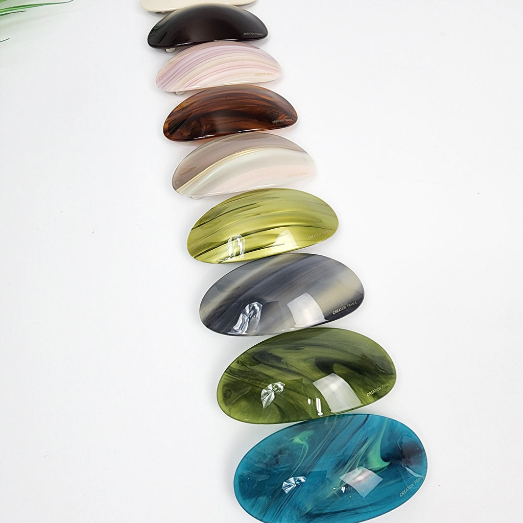Cellulose acetate oval hair barrette featuring tortoise shell and marble patterns. Medium 3.5 inch curved automatic clip designed for secure half-up hairstyles. A set of ten oval-shaped hair clips in various colors, including brown, white, green, blue, and gray. The clips have a glossy finish and a marbled pattern.