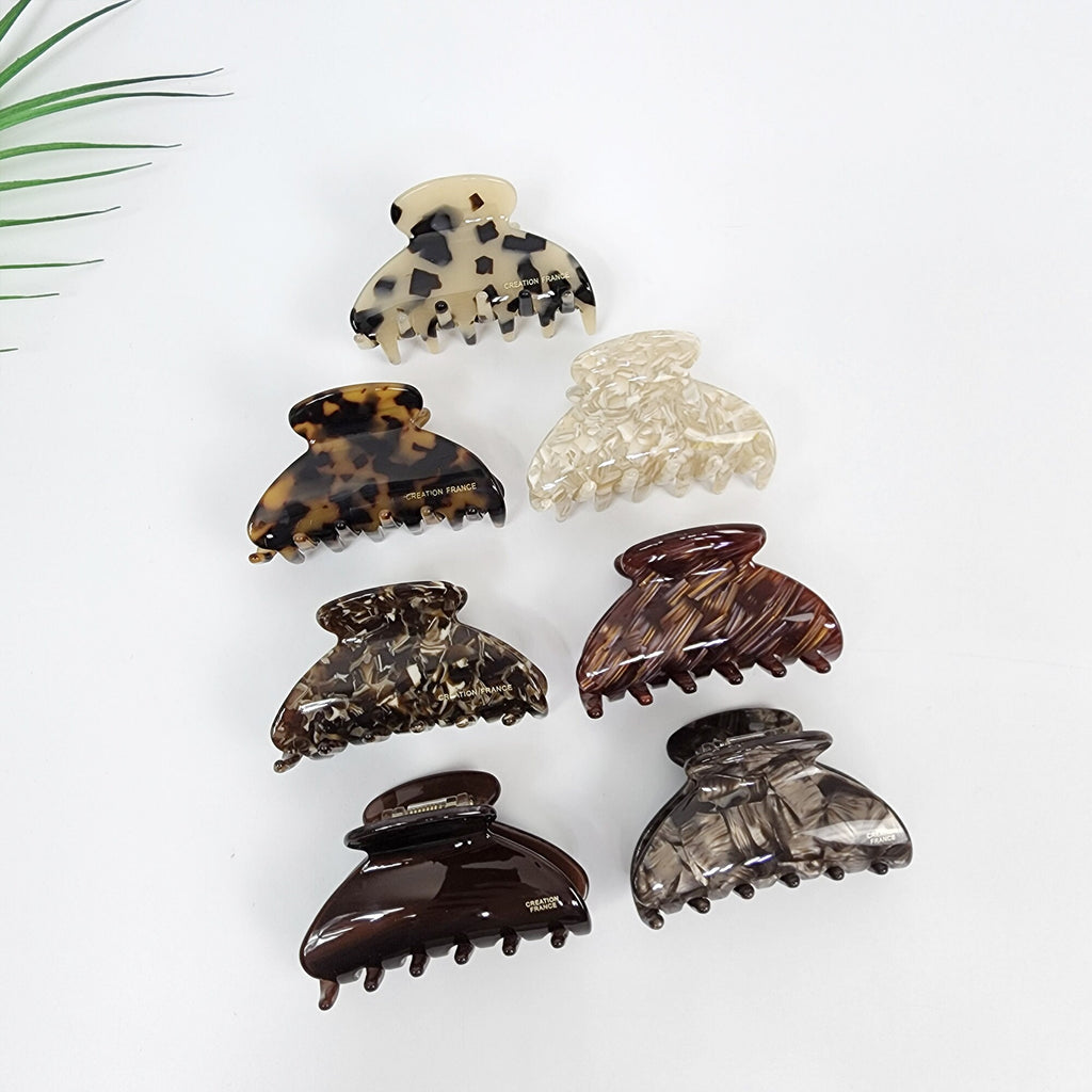 Cellulose acetate half moon hair claw clip featuring tortoise shell and marble patterns. Small 2.6 inch jaw clip designed for secure half-up hairstyles. Six different patterned hair clips. The clips are made of brown, black, and white plastic. The clips have a claw shape with five prongs. The clips are all different patterns, including tortoise shell, leopard print, and marble.