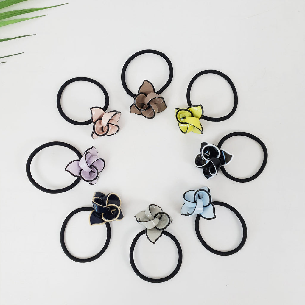 Glossy cellulose acetate flower hair tie in pastel colors. Cute blooming botanical ponytail holder with black elastic band for girls birthday gifts. Korean fashion accessory. Eight black hair ties with different colored flower embellishments. The flowers are in the colors of light pink, brown, yellow, black, light blue, dark blue, and gray.