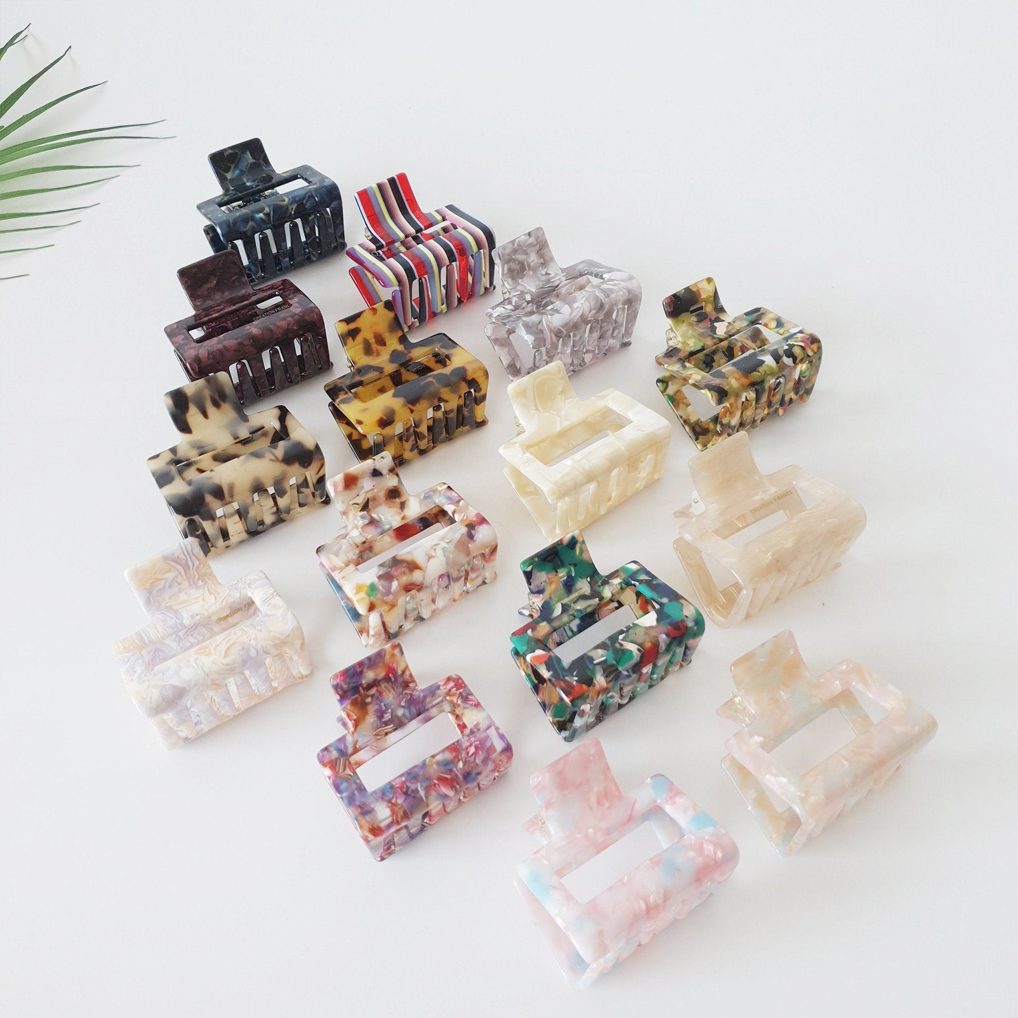 Rectangular cellulose acetate hair claw clip, marble square jaw clip for half-up hairstyles, sturdy Korean hair accessory for women birthday gift. A collection of 16 assorted hair clips. The clips are made of plastic and have a variety of colors and patterns, including black, brown, white, red, green, blue, and yellow. The clips are all in the shape of a rectangle with a small, curved handle on one side.