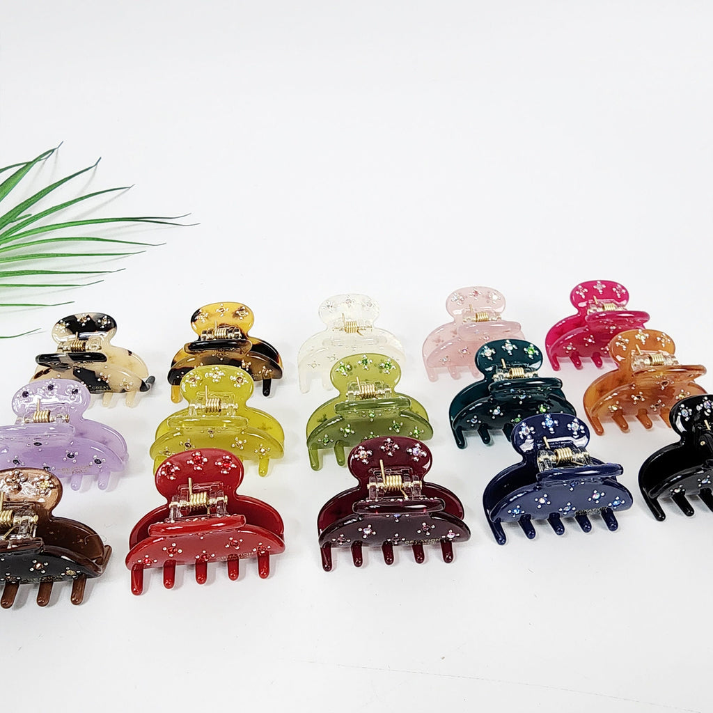 Small cellulose acetate hair claw with sparkling rhinestones. Mini half-moon jaw clip in tortoise and solid colors for bangs or side hair styling.  A collection of twelve colorful plastic hair clips with a star pattern. The clips are arranged in two rows of six. The clips are in various colors including purple, red, green, blue, brown, and pink.