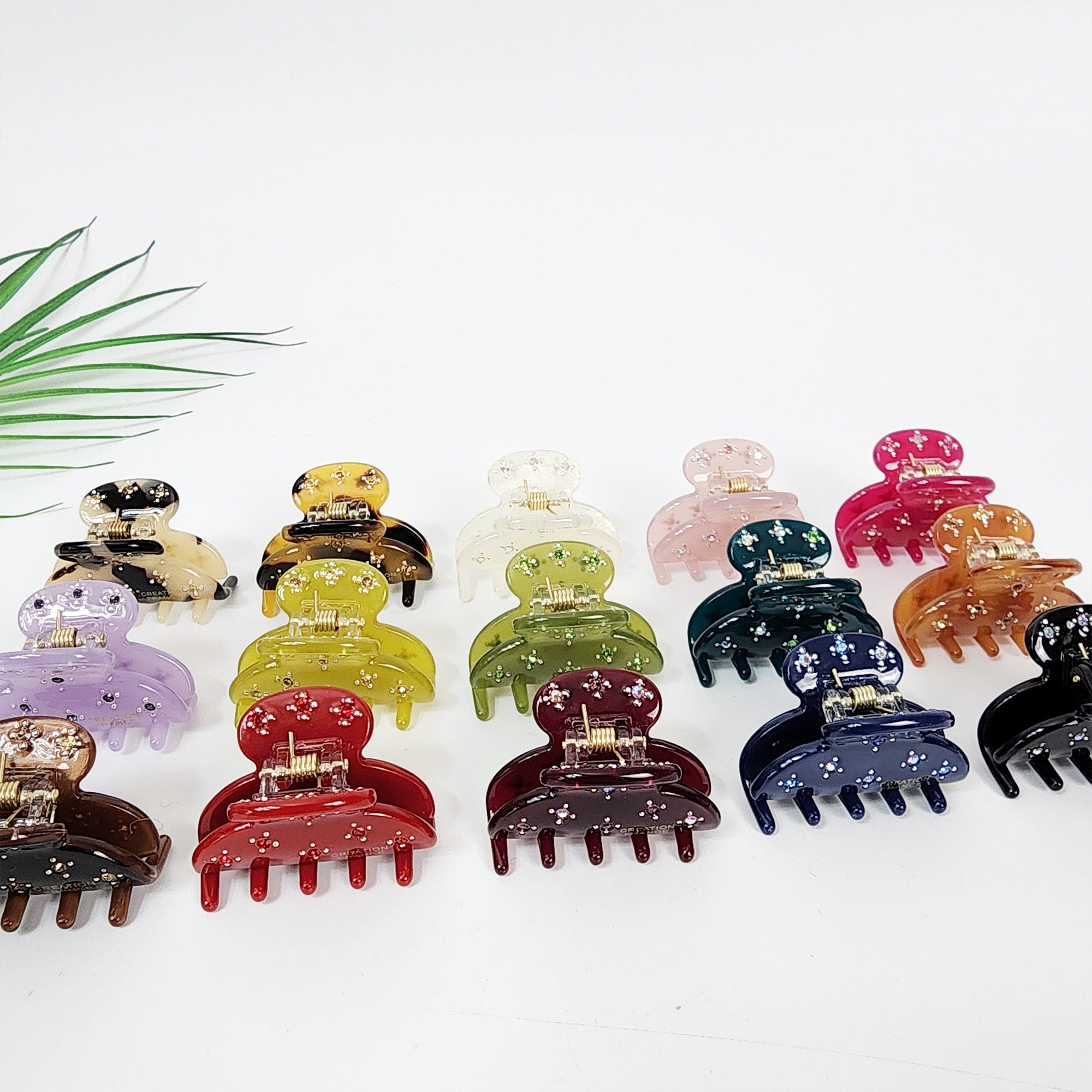 Small cellulose acetate hair claw with sparkling rhinestones. Mini half-moon jaw clip in tortoise and solid colors for bangs or side hair styling.  A collection of twelve colorful plastic hair clips with a star pattern. The clips are arranged in two rows of six. The clips are in various colors including purple, red, green, blue, brown, and pink.
