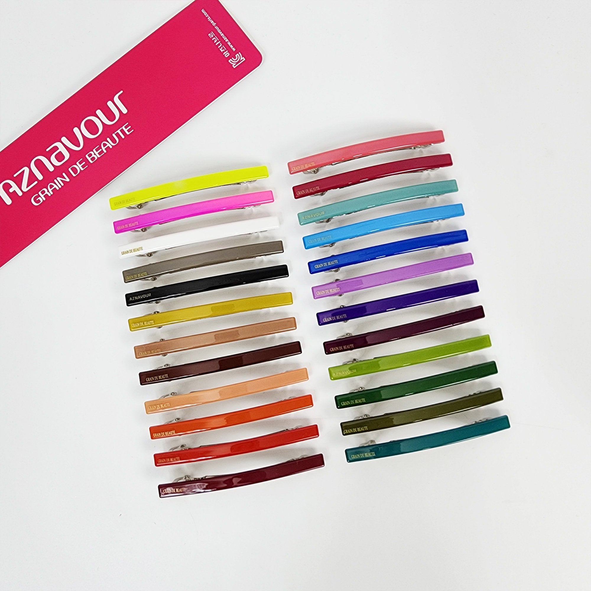 Long skinny cellulose acetate barrette in vivid colors. Minimalist glossy rectangular hair clip for side bangs or half up styling. A set of 18 hair clips in various colors including red, orange, yellow, green, blue, purple, brown, and white. The clips are all the same size and shape, and they have a shiny finish. The clips are arranged in rows, with each row containing a different color. The clips are labeled with the words 'GRAIN DE BEAUTE'.