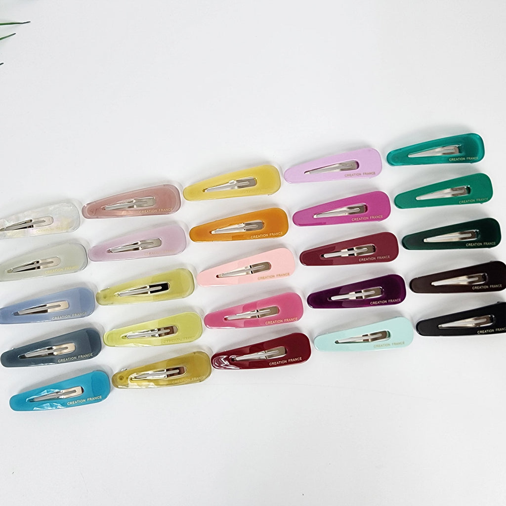 Triangle shaped cellulose acetate snap clip in pastel and solid colors, 2.2 inch minimalist barrette for side bangs, cute hair accessory for girls and women. Twenty-four assorted plastic hair clips in various colors, including yellow, pink, green, blue, red, and brown. The clips are all rectangular in shape and have a silver metal clasp. The clips have the words 'CREATION FRANCE' printed on them.