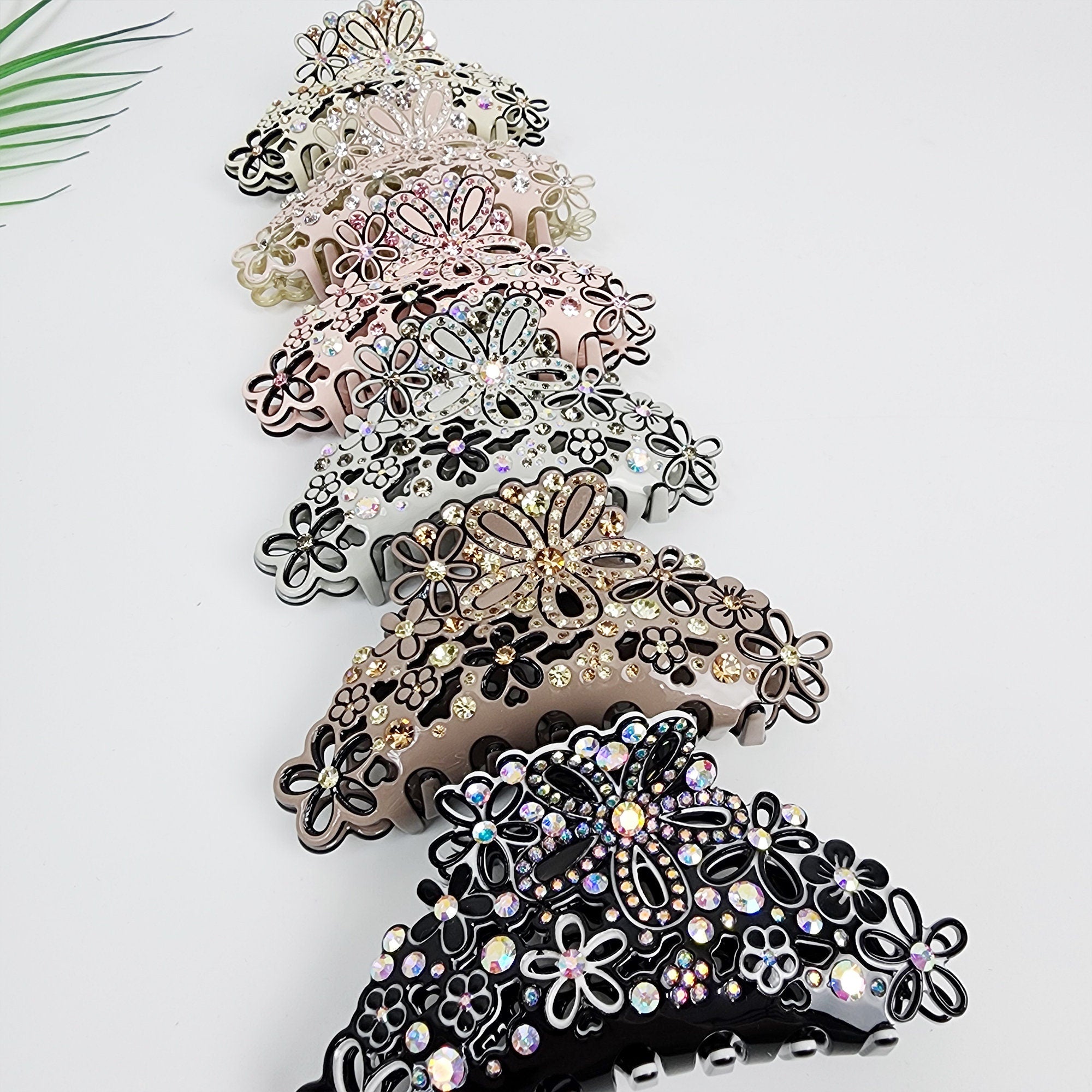 Rhinestone floral hair claw clip, large acetate clamp for thick hair, sparkly crystal wedding accessories, elegant Korean fashion gift. A set of seven hair claw clips with a floral design. The clips are made of plastic and are decorated with rhinestones. The clips are arranged in a row, with the largest clip at the bottom and the smallest clip at the top. The clips are in various colors, including black, brown, white, and pink.