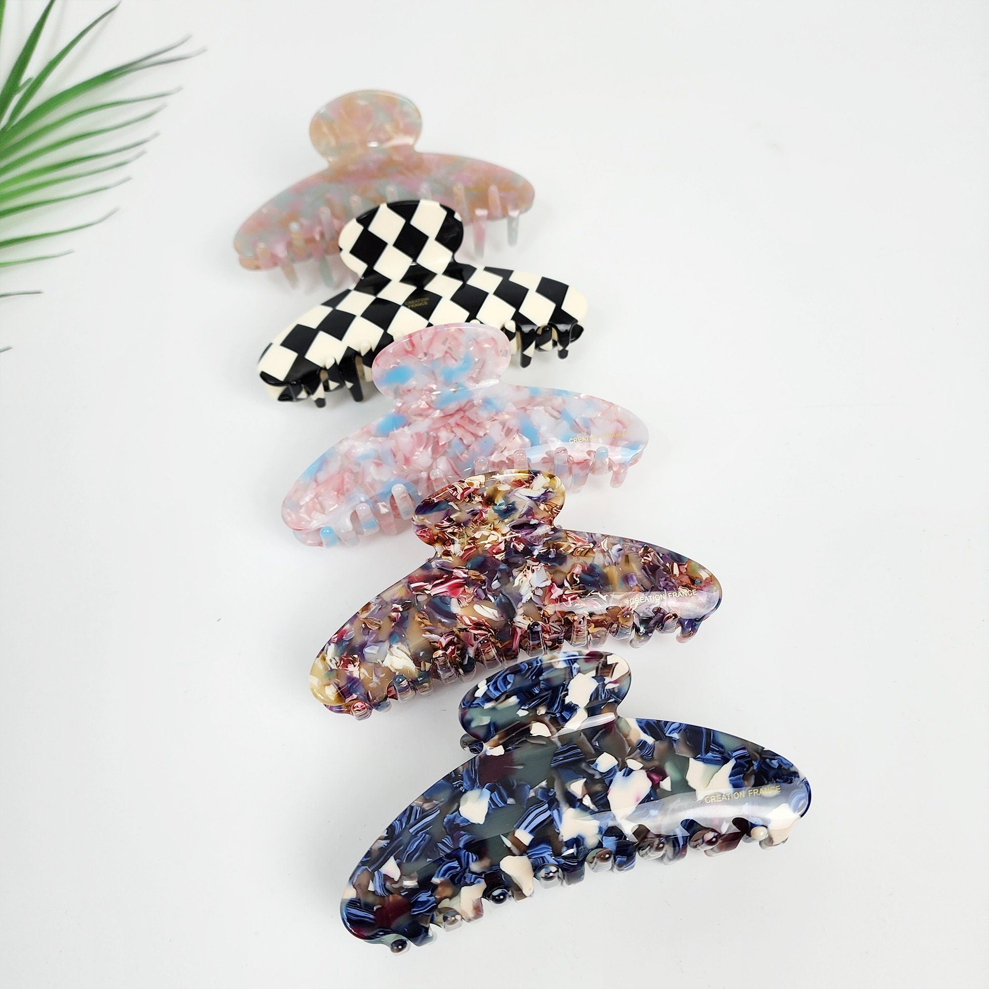 Cellulose acetate hair claw clip featuring marble, tortoise shell, and checkerboard patterns. This 4.3 inch long semi-circle jaw clip provides a secure hold for french twist updos and thick hair types.