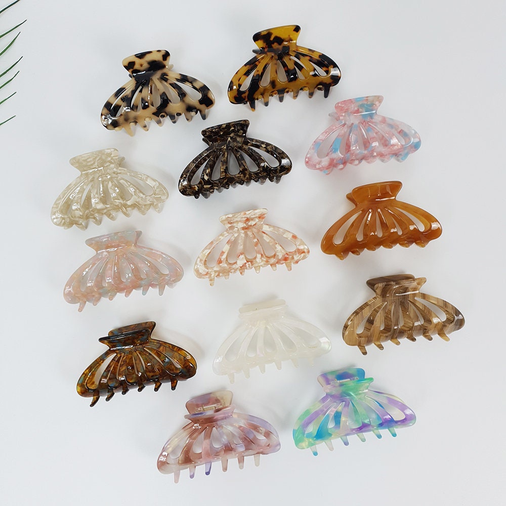 Cellulose acetate shell shaped hair claw in tortoise and marble patterns. 3.5 inch fan hair clip perfect for half up styles and securing fine to medium hair. A collection of twelve hair clips in various colors and patterns. The clips are made of plastic and have a claw-like design. The colors include brown, beige, pink, and blue. The patterns include tortoise shell, marble, and floral.