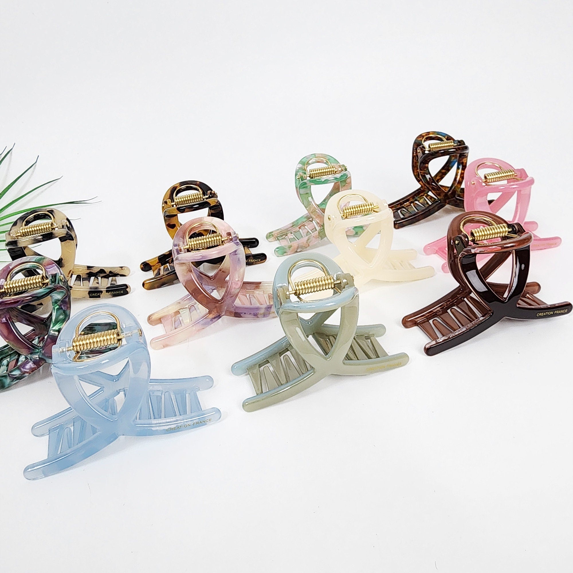 Medium cellulose acetate twist hair claw with durable U-shaped spring mechanism. No-glue design in pastel and tortoise shell colors for half-up hairstyles. A set of eight hair clips in various colors including brown, pink, blue, green, and beige. The clips are made of plastic and have a unique design with a curved shape and a spring mechanism. The clips are designed for holding hair in place.