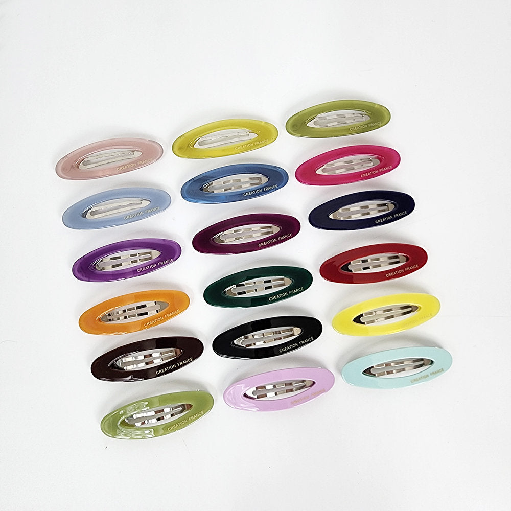 Glossy cellulose acetate oval snap clips in solid red and assorted colors. Minimalist French style small barrettes for side bangs. Cute hair accessories for women and toddlers. A collection of 18 oval-shaped hair clips in various colors including yellow, green, blue, purple, pink, red, orange, brown, and black. Each clip has a silver metal bar with a 'CREATION FRANCE' logo.