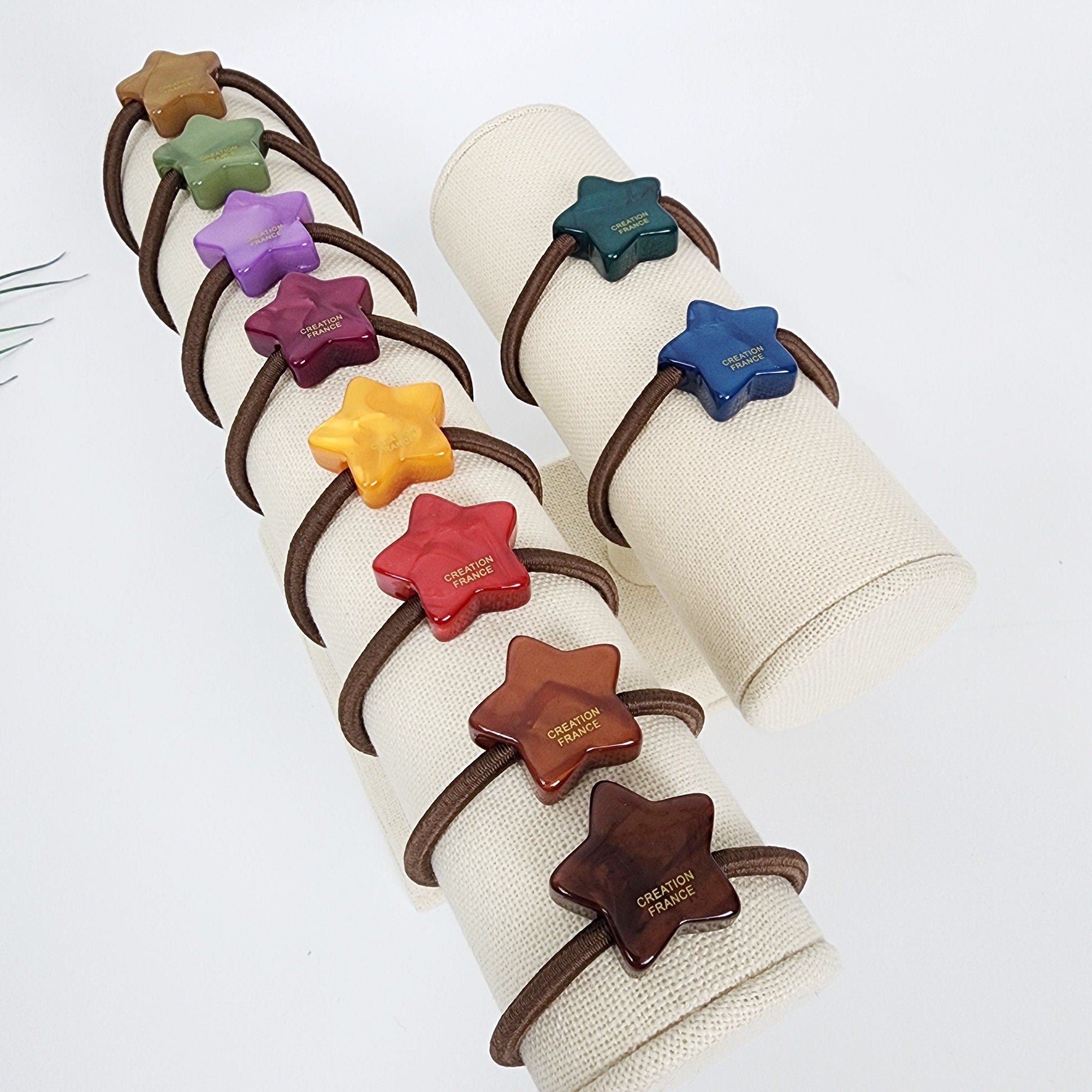 Cellulose Acetate star shaped hair accessory in earth tone and bright colors minimalist geometric ponytail holder for birthday gift. A set of eight star-shaped hair ties on a display stand. The hair ties are made of different colors, including green, purple, red, orange, yellow, and brown. Each hair tie has the words 'CREATION FRANCE' printed on it.