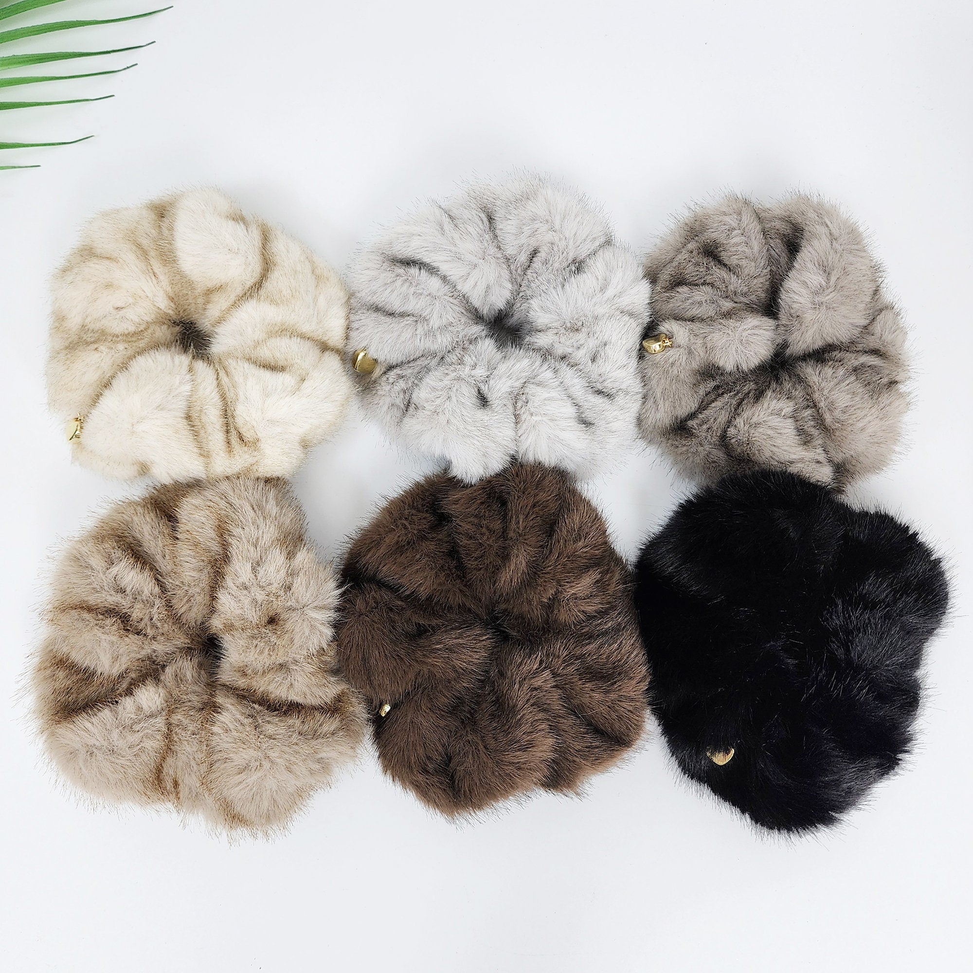 Soft faux mink hair tie in beige gray and black. Fluffy winter ponytail holder with gold heart charm. Cute Korean hair accessory. Six fuzzy hair scrunchies in different colors and patterns. The scrunchies are arranged in a circle on a white surface. The scrunchies are light brown with a striped pattern, gray, dark brown, black, and two more light brown with a striped pattern.